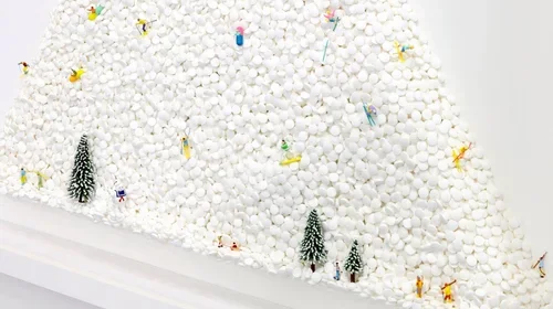 A large pile of white cotton balls with small colorful toys and miniature Christmas trees scattered on top.