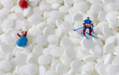 Miniature hockey player figurine skating on a bed of white mini marshmallows with a tiny toy train, a small toy figure, and a red candy in the background.