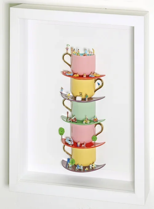 Stacked colorful teacups with miniature figurines and tiny trees inside them, arranged vertically within a shadow box.