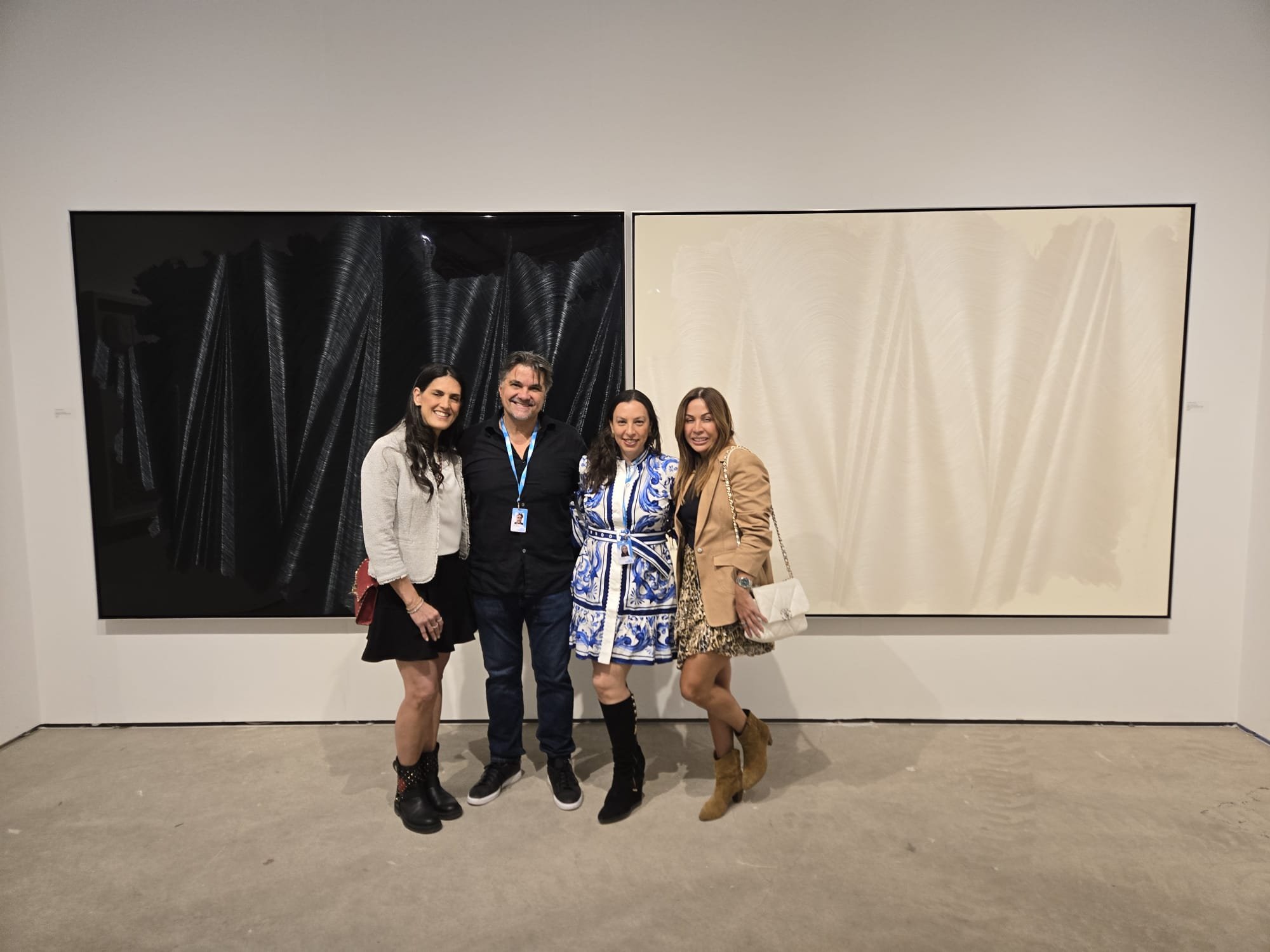 Four people standing in front of two large abstract paintings at an art gallery, smiling and posing for the photo.