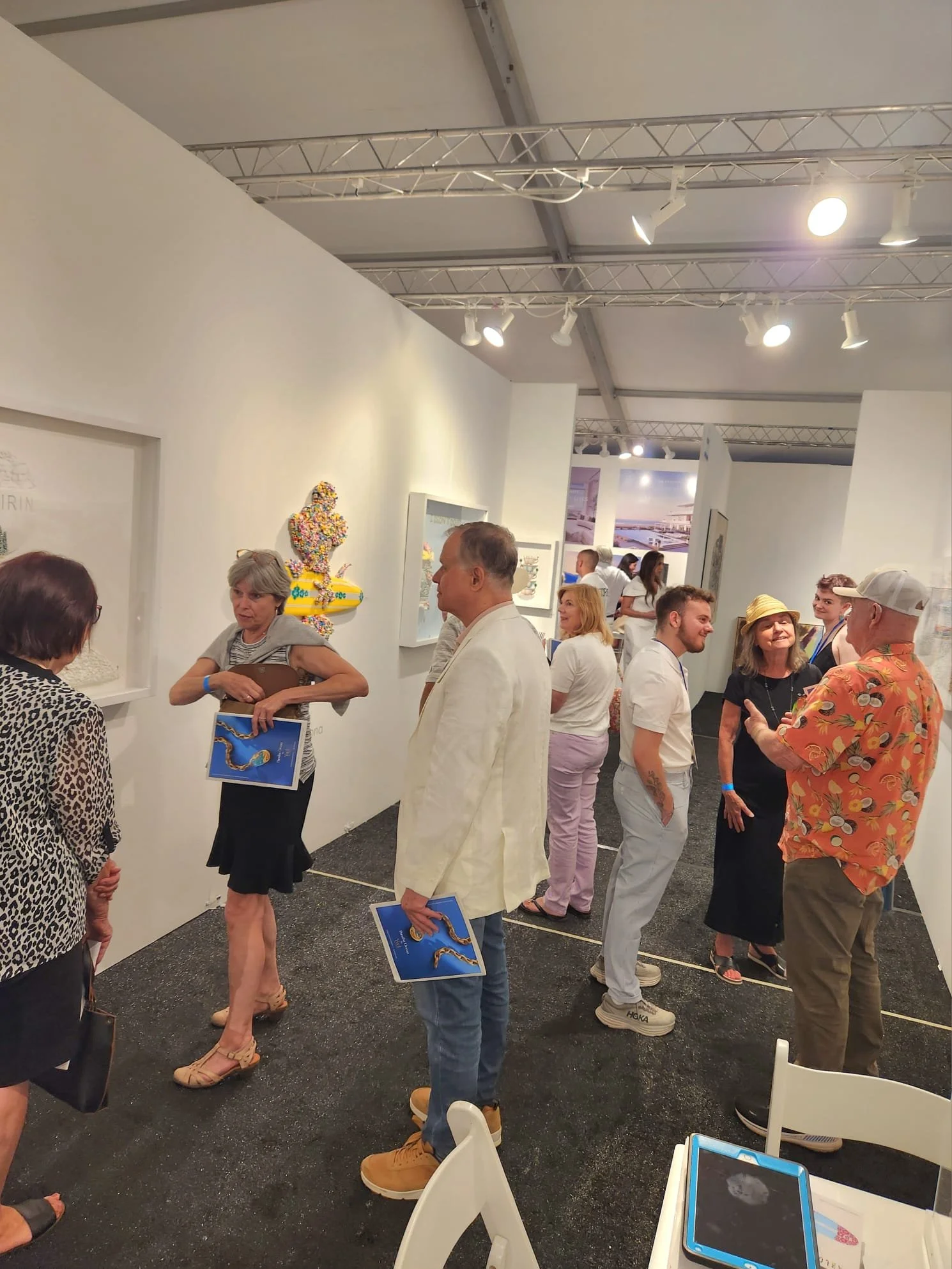 People attending an art gallery, looking at artwork on the white gallery walls, and engaging in conversations.