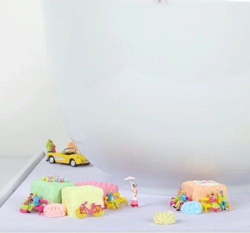 Small toy beach scene with miniature toys, colorful towels, and a small yellow car on a white surface.