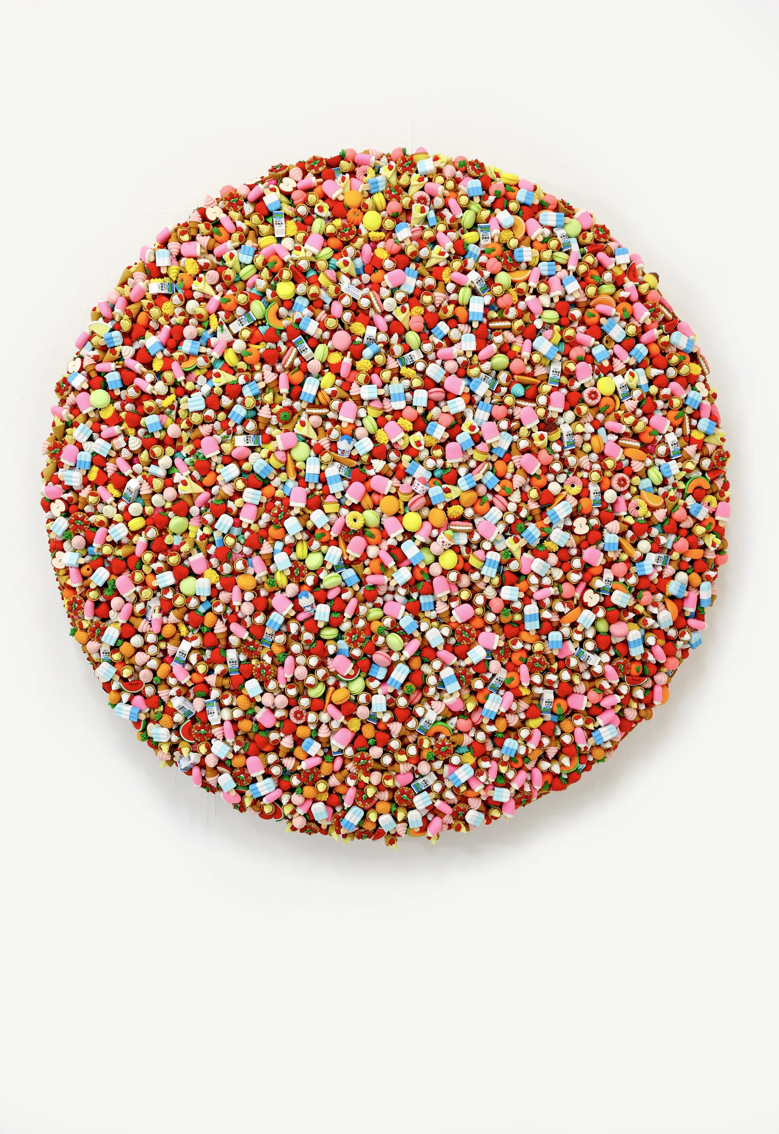 Round art piece made from a variety of colorful tiny beads and miniature objects on a white background.
