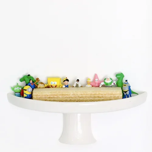 Cake decorated with colorful Toy Story character figurines on a white cake stand against a white background.