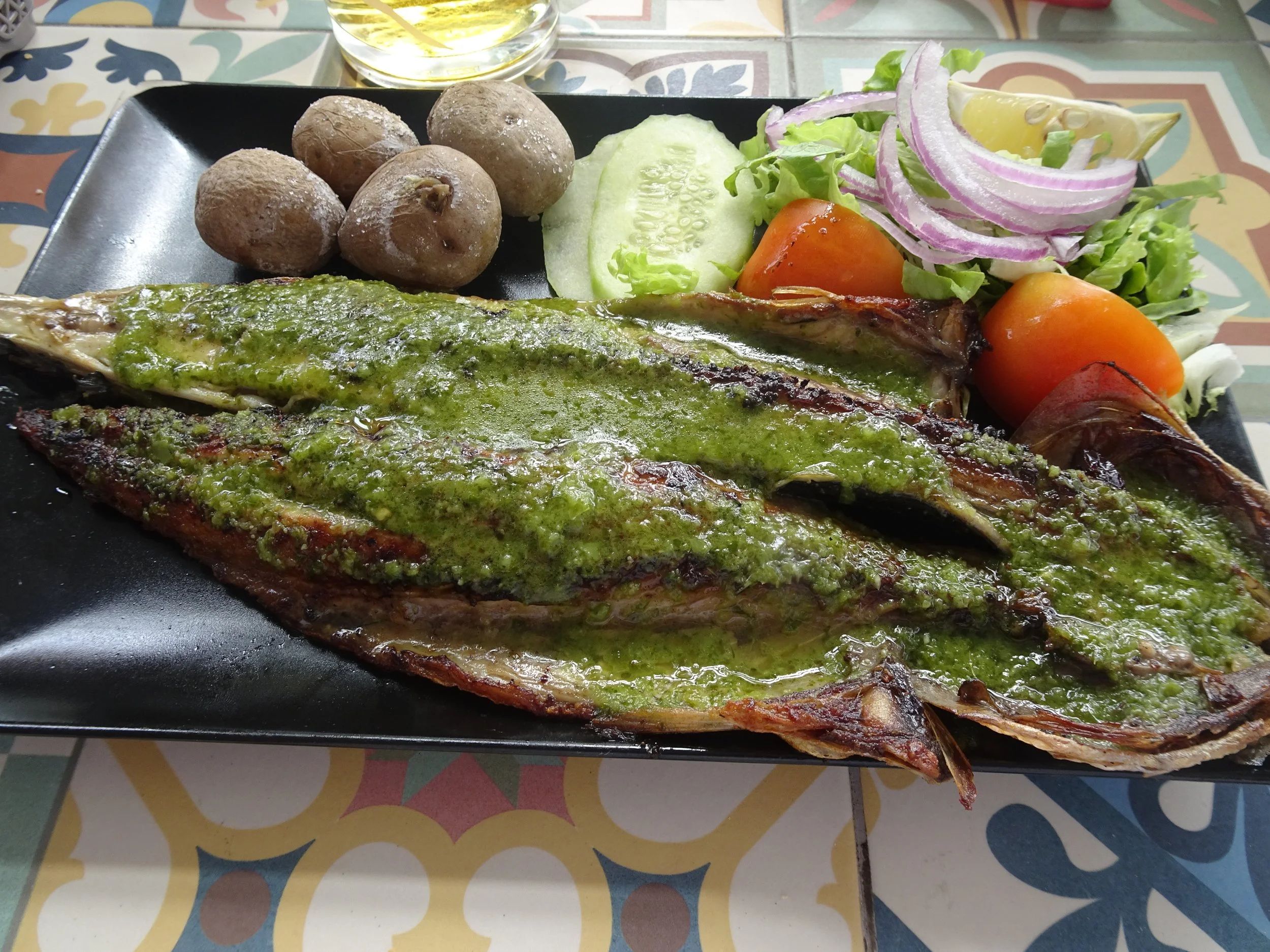 Fisch mit Kräuterpesto und Gemüse auf einem schwarzen Teller
