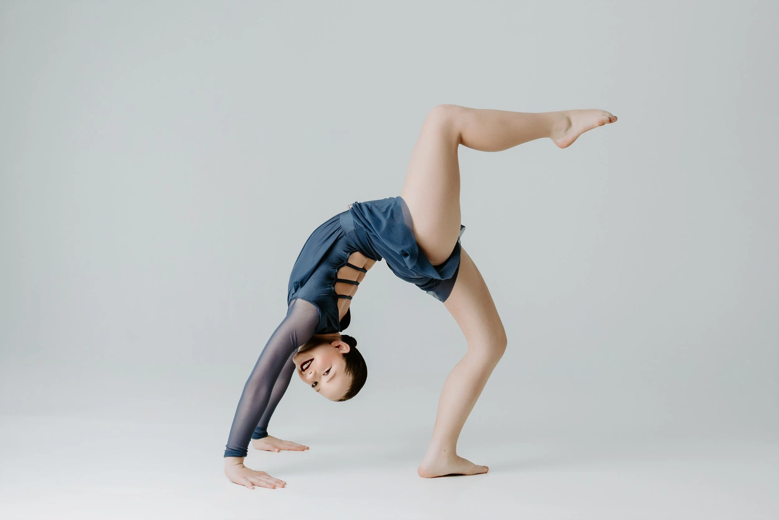 Two children performing a yoga pose, with one bending backwards and the other inverted in a handstand, set against a plain gray background.