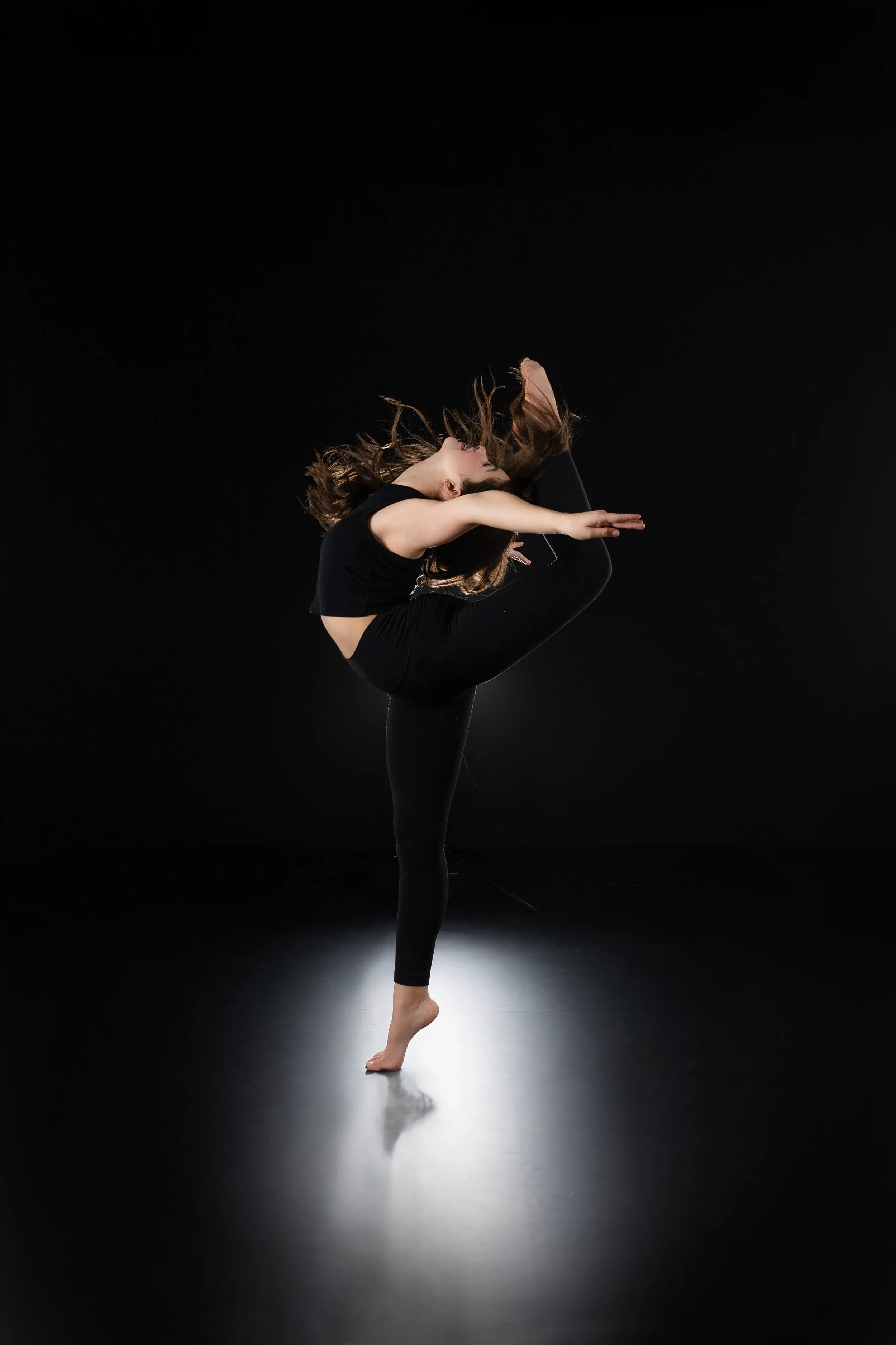 A woman dressed in black performing a dance pose on a dark stage.
