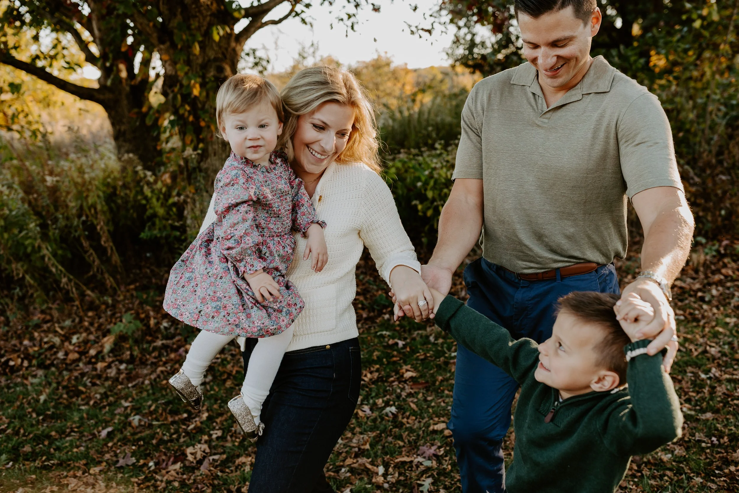 A family enjoying an outdoor gathering in autumn, with children and parents holding hands and smiling.