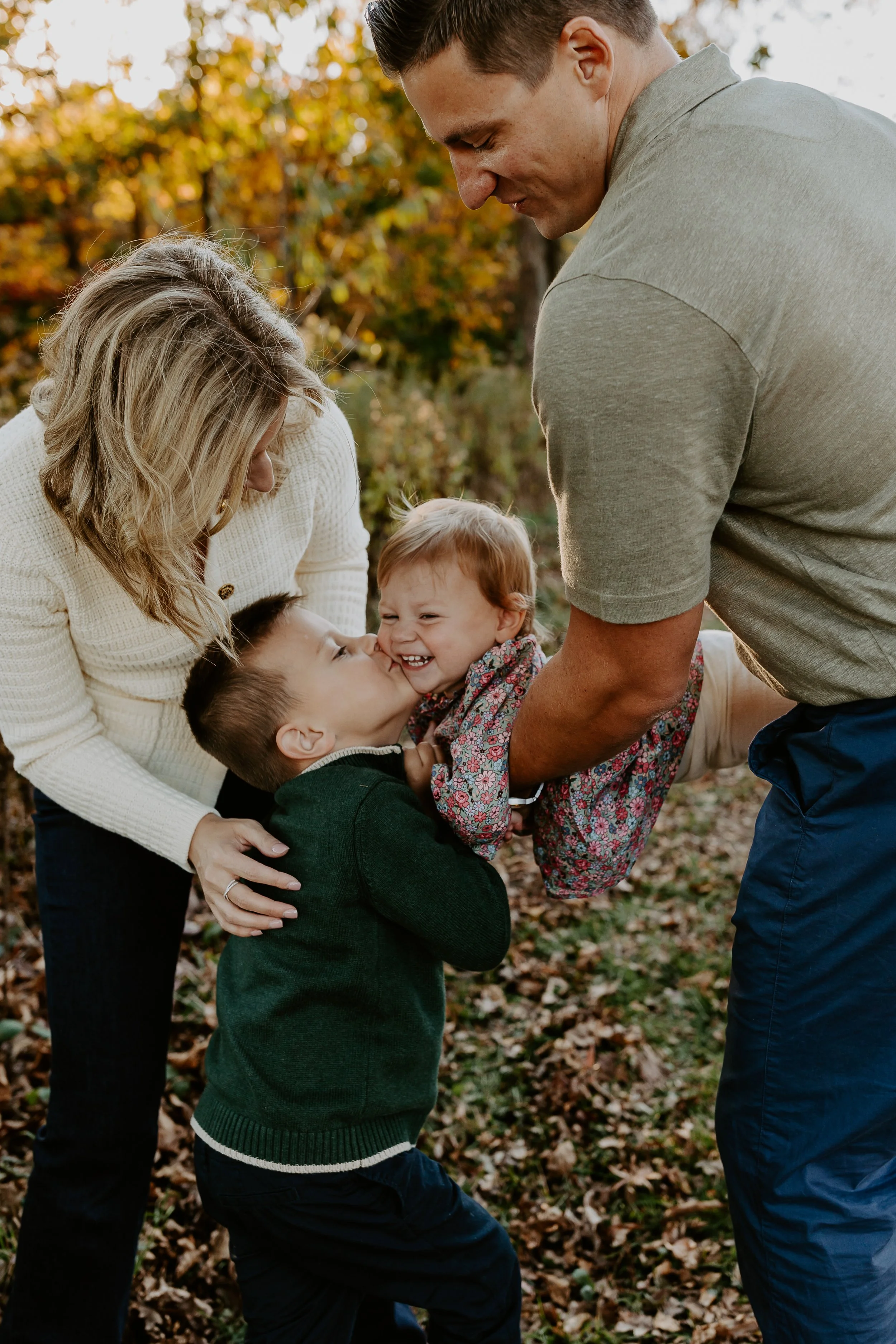 Family playing and laughing outdoors during fall with autumn leaves on the ground.