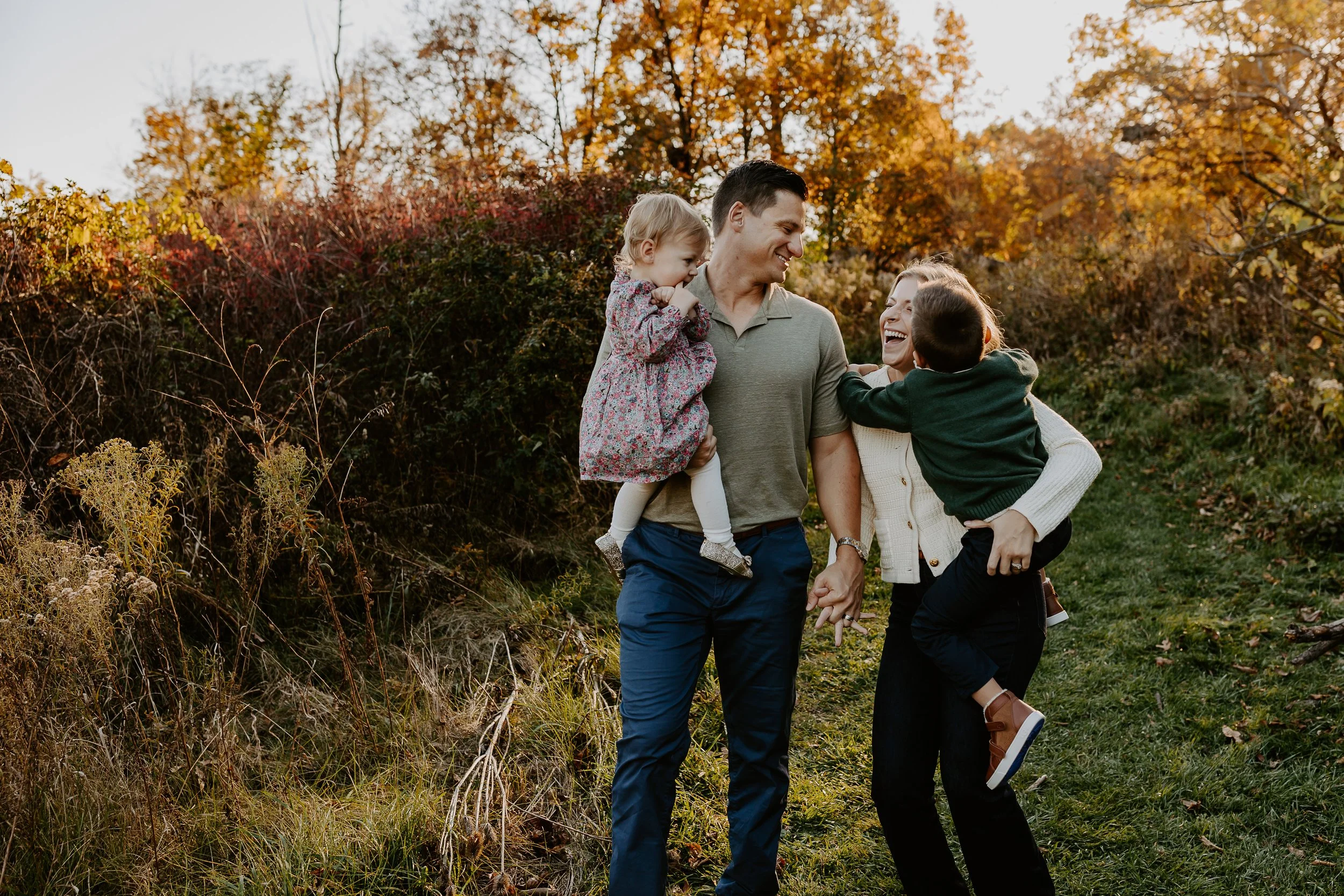 Family of four sharing a joyful moment outdoors during autumn, surrounded by colorful fall foliage and tall grass.