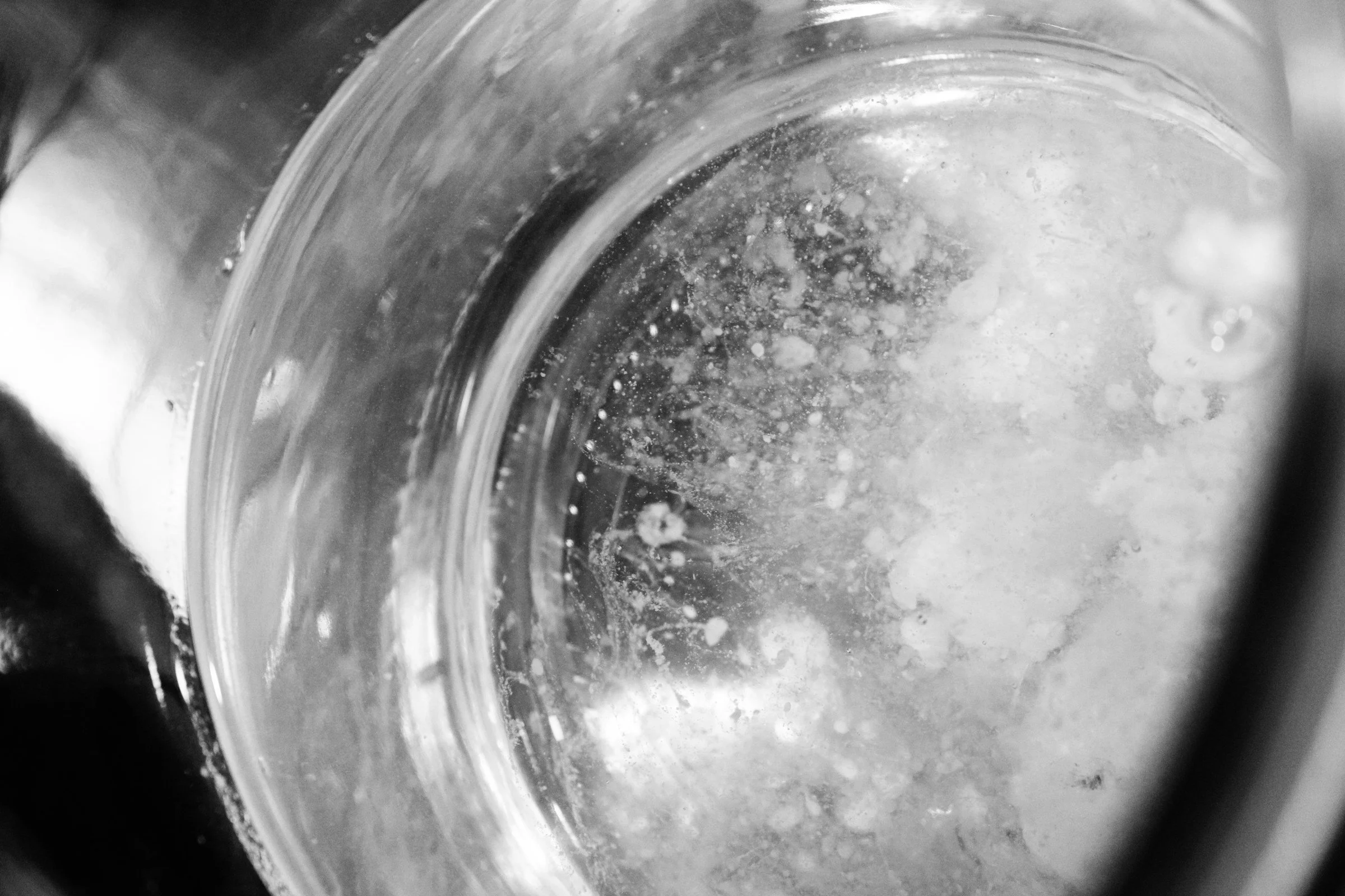 Close-up view inside a glass with some liquid and bubbles, taken from a tilted angle in black and white.