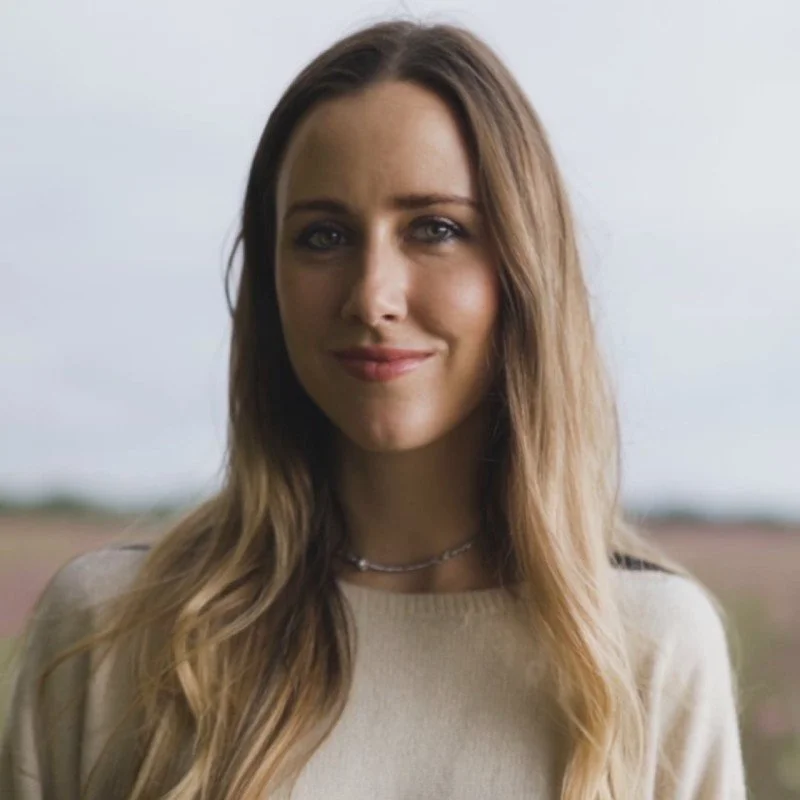 A young woman with long wavy light brown hair, smiling in an outdoor setting with a blurred landscape background. Laura is a business owner and participated in Leadership That Lasts: A Retreat For Women in November 2025.