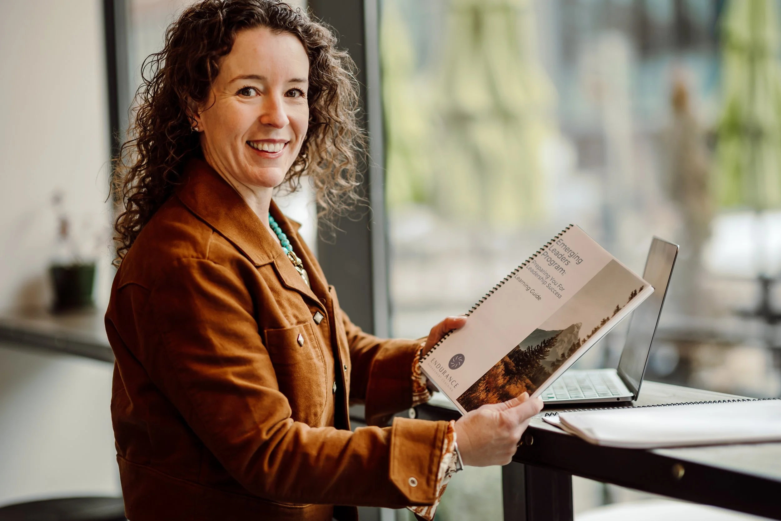 A flat lay of a workspace with a white computer keyboard, white wireless mouse, a notebook with lined paper and a pen, a digital drawing tablet with a stylus, and a potted plant, all on a yellow surface.