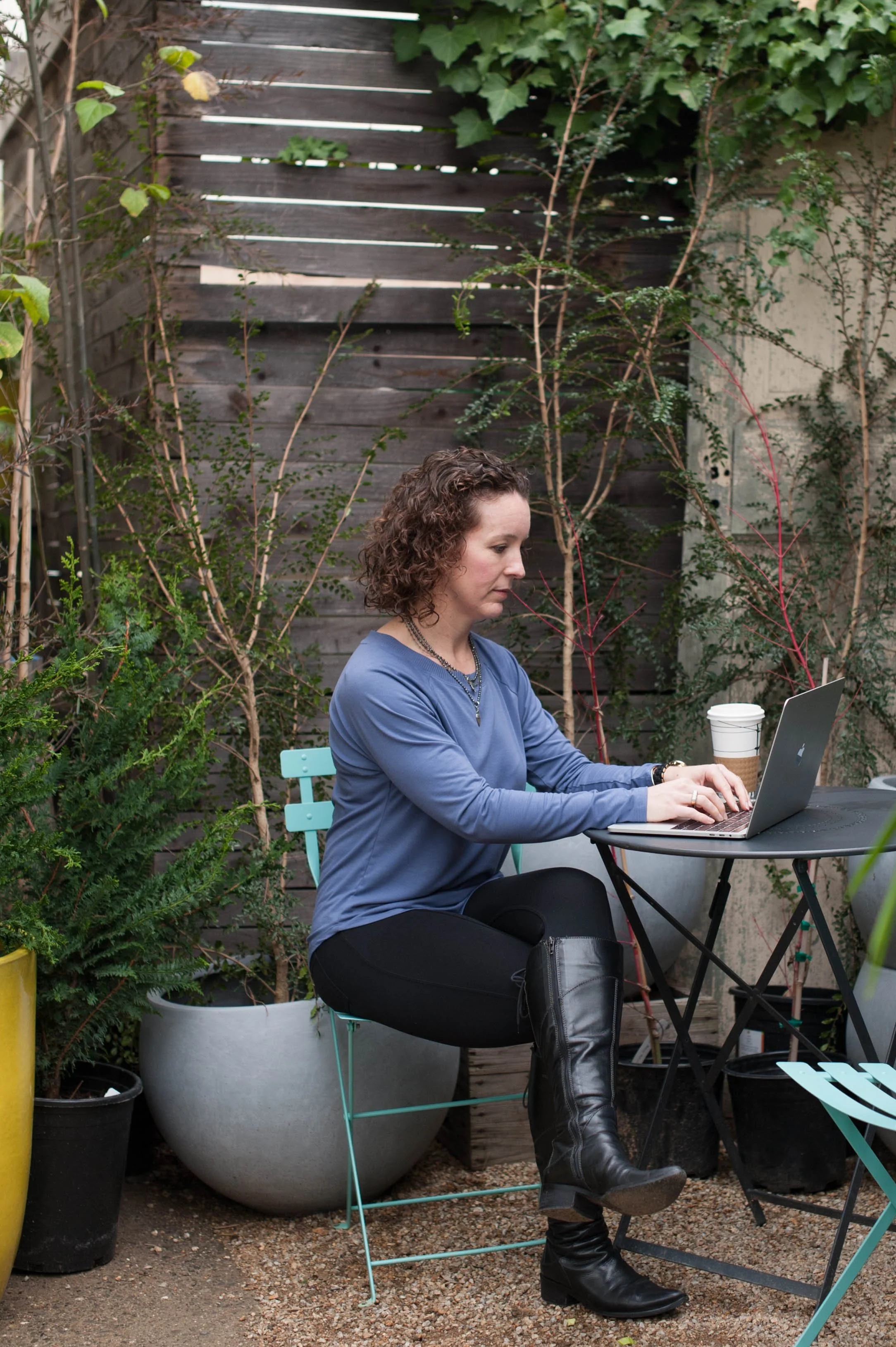 An image of Katie O'Brien Ceccarini on her laptop while sitting at a table in a garden. Katie is the founder of endurance management coaching, a certified leadership and executive coach, and the award-winning author of Fearless Feedback