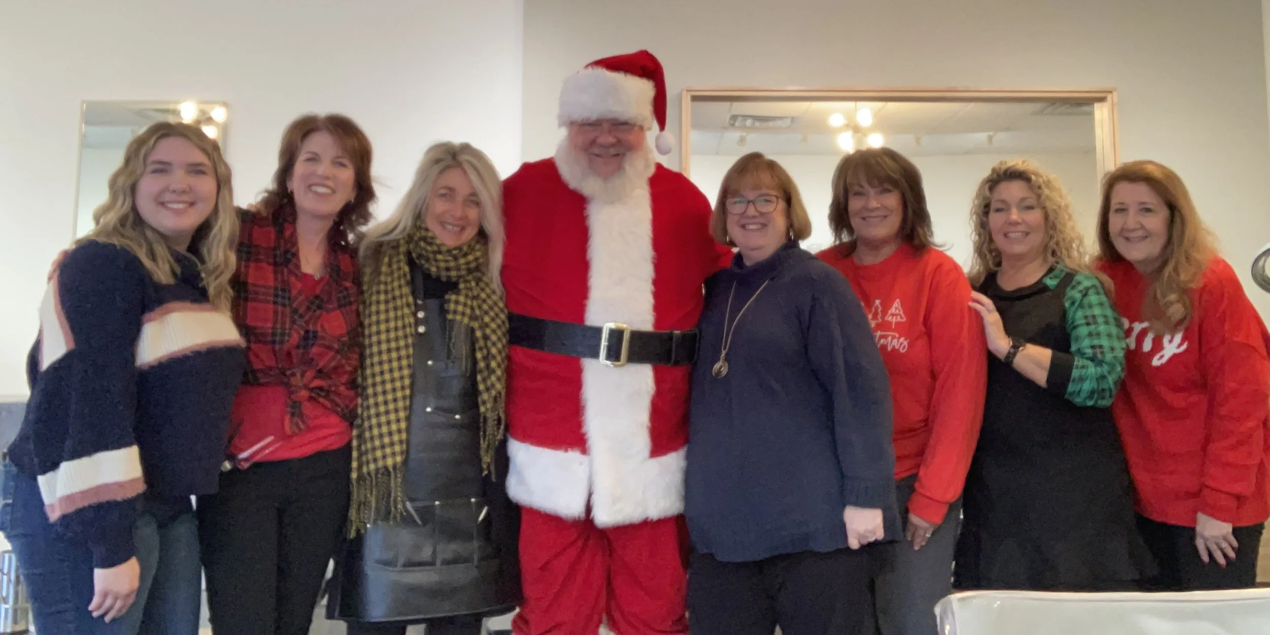Group of women and a person dressed as Santa Claus celebrating Christmas, posing together indoors.