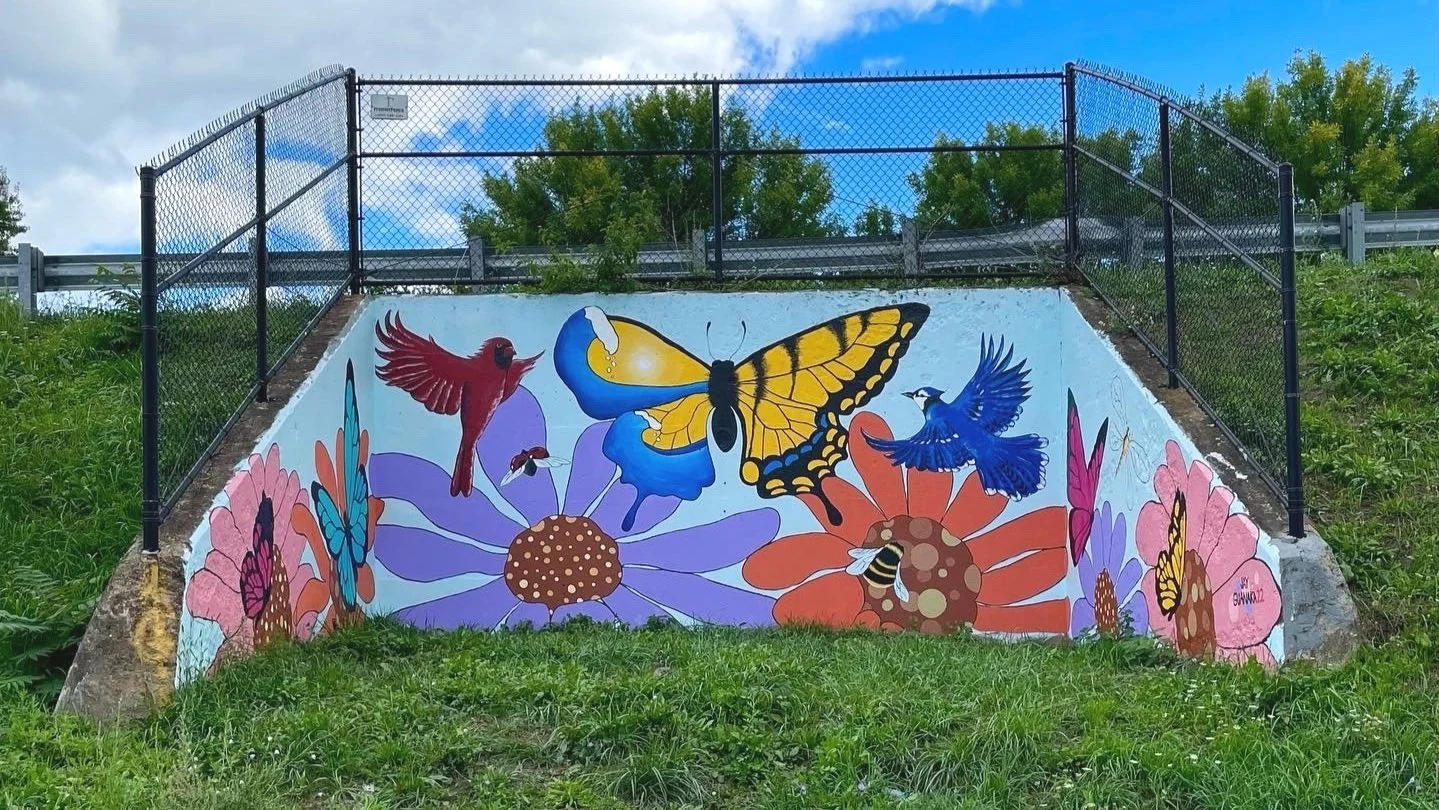 Retaining wall on grassy hillside painted with mural of flowers, butterflies, and birds