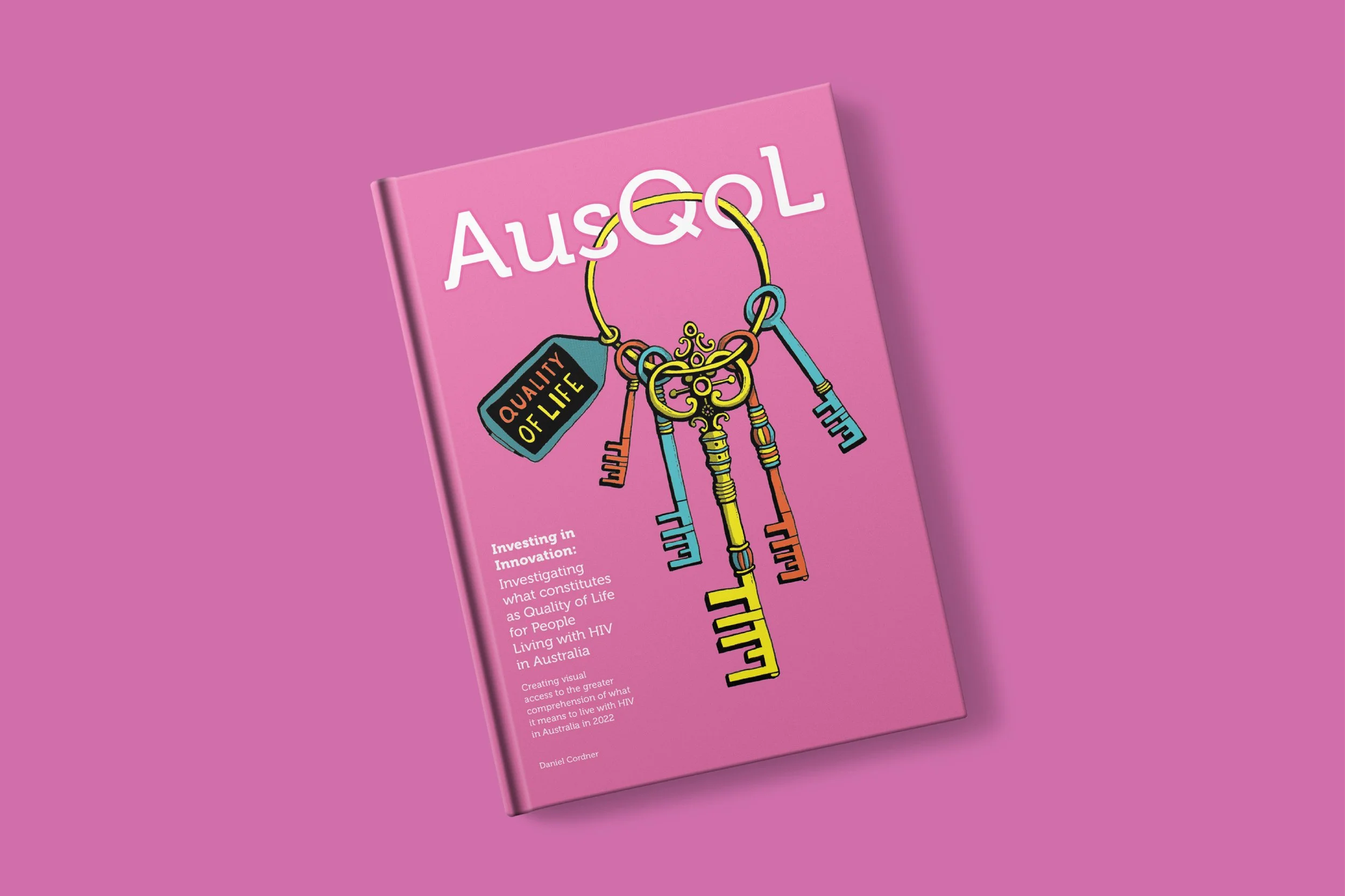 A pink hardcover book titled 'AusGOAL' displays a colorful illustration of a keyring with five keys and a tag that says 'Quality of Life'. The background is solid pink.