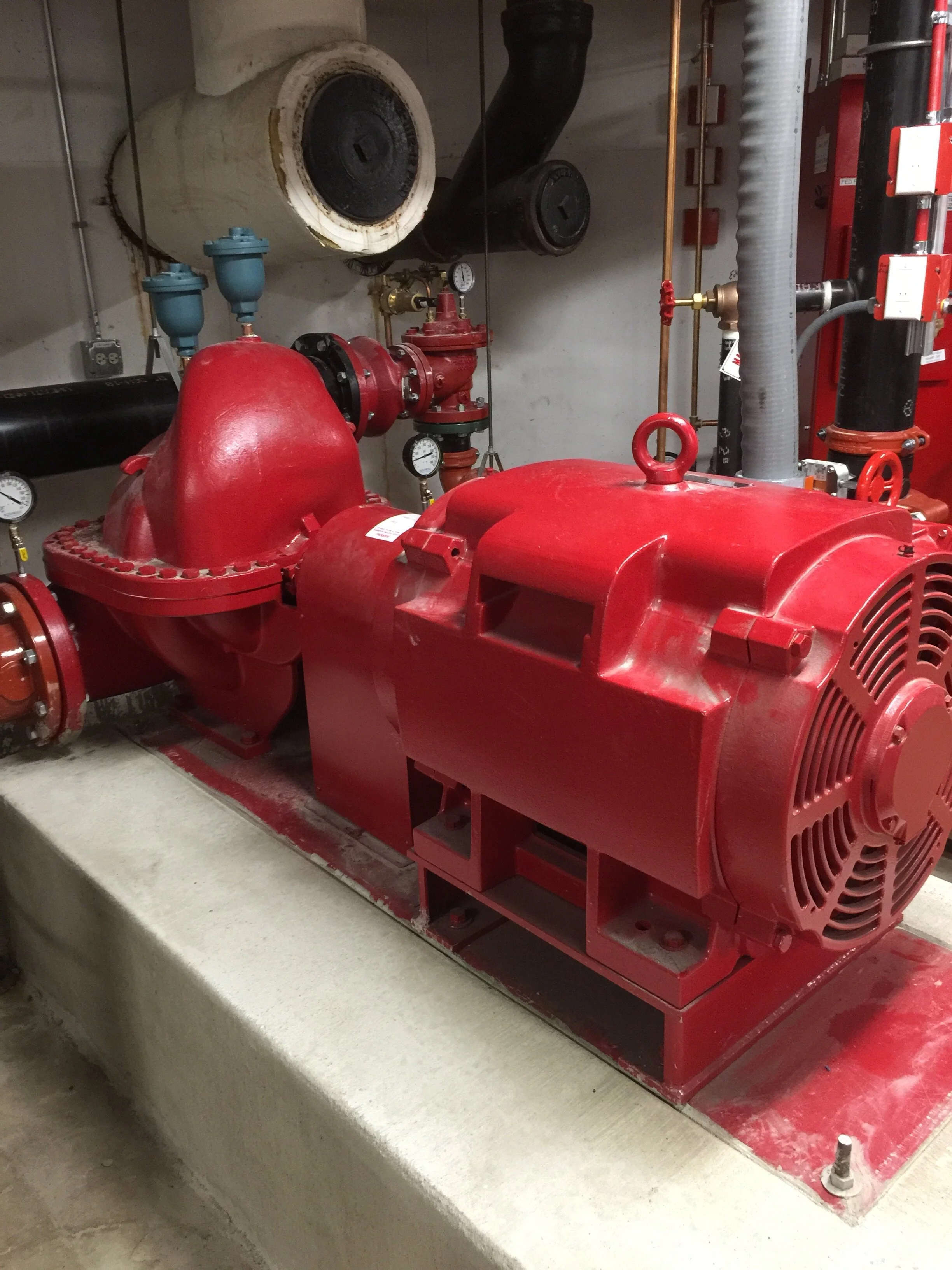 Red fire pump system with various pipes, gauges, and valves in an industrial setting.