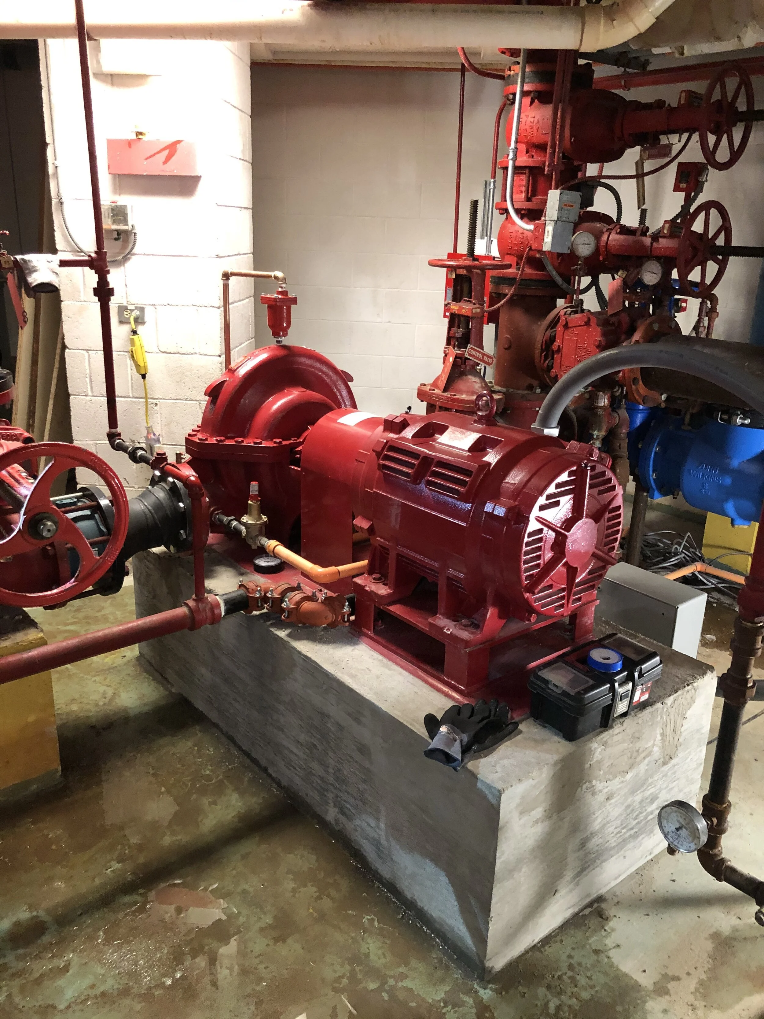 Red fire pump on a cement base, a casing relief valve and valves and piping in the background