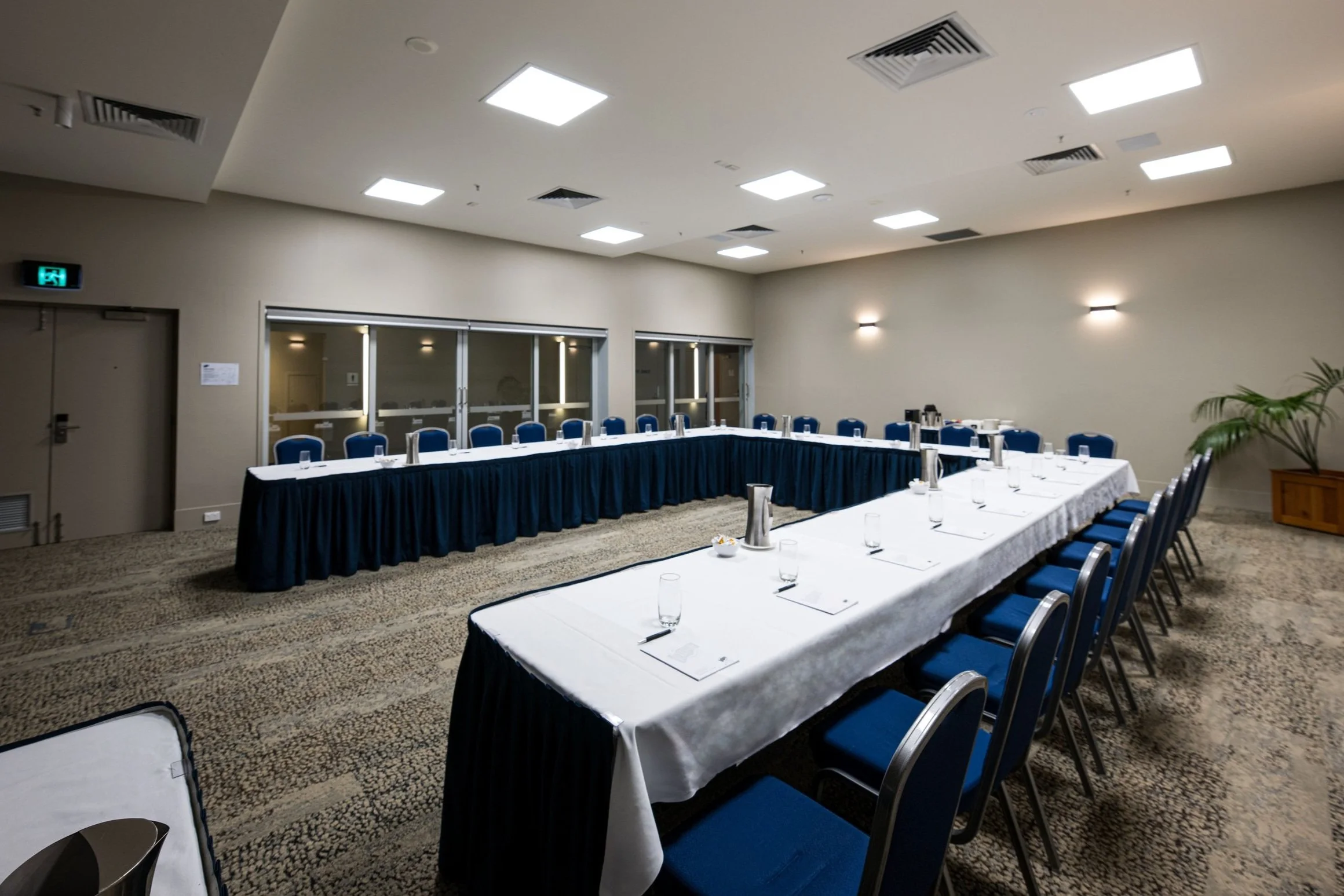 U shaped table set for a large conference. Set in the Wapping Room against wall of glass sliding doors