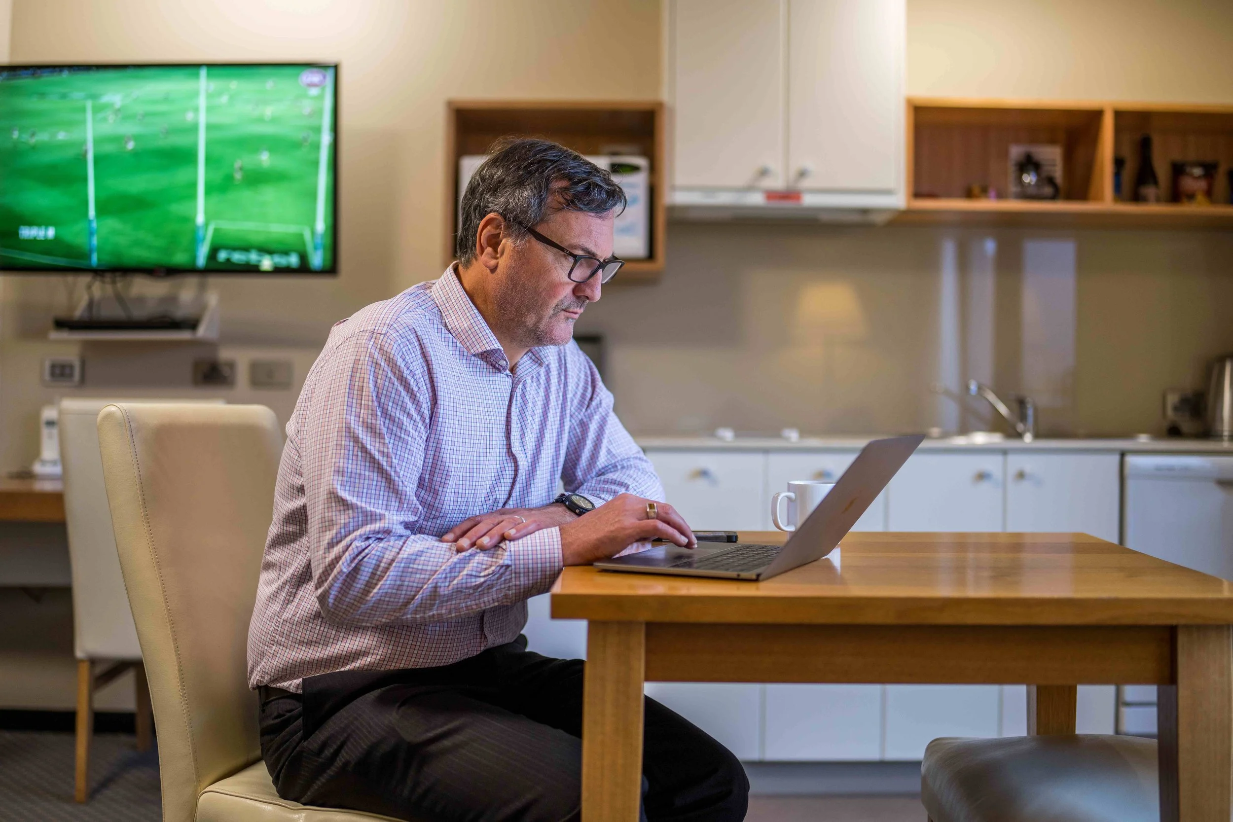 Corporate Traveller working at study and dining space near kitchenette in an apartment with TV on