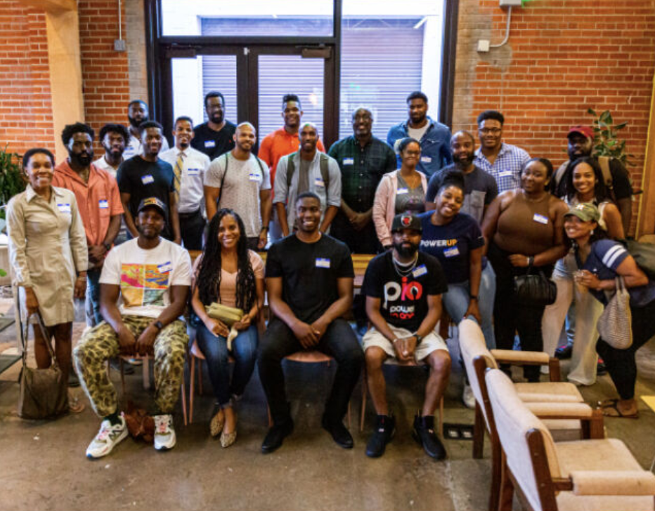 Group of diverse people posing for a photo in a room with brick walls and large windows.
