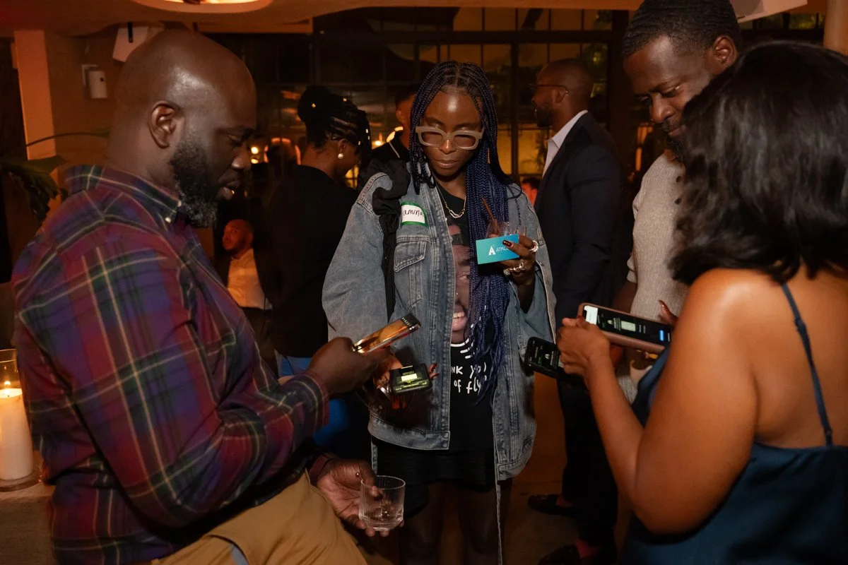 Group of people at a social gathering, looking at their smartphones in a warmly lit indoor setting.