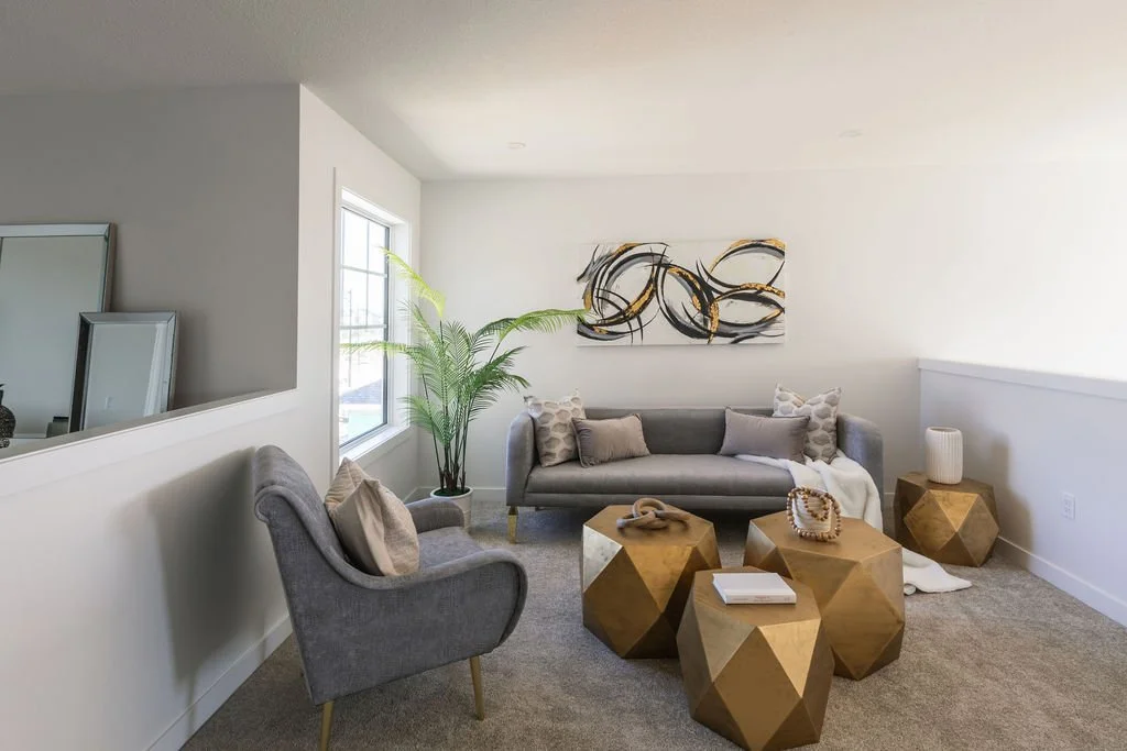 Photo of a carpeted living room with grey sofas and throw pillows, a houseplant, and gold designer tables