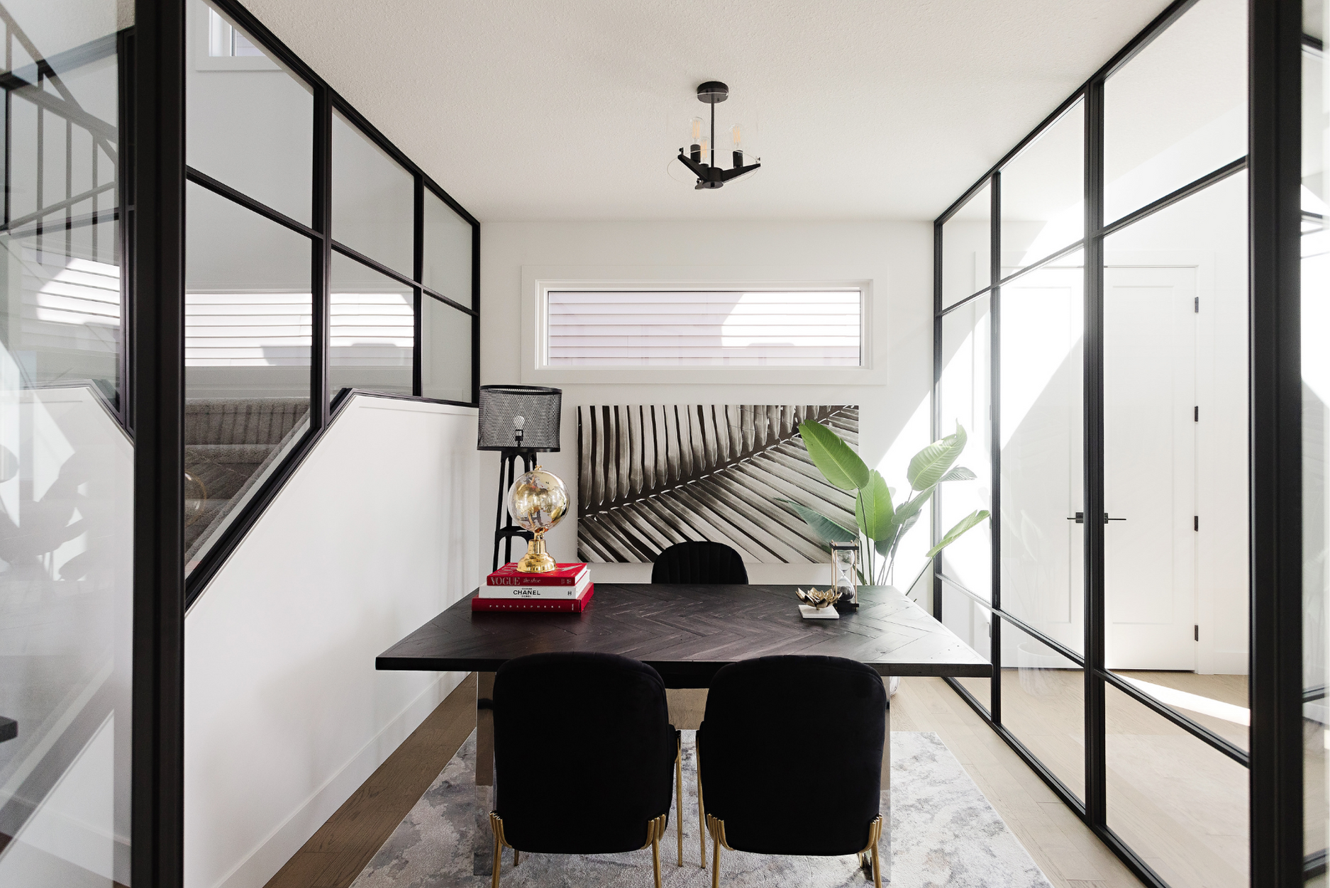 Picture of an IT office design with a solid wood table at the center, paired with black chairs, ambient lighting, floor-to-ceiling glass, a potted plant, and curated artwork in the background