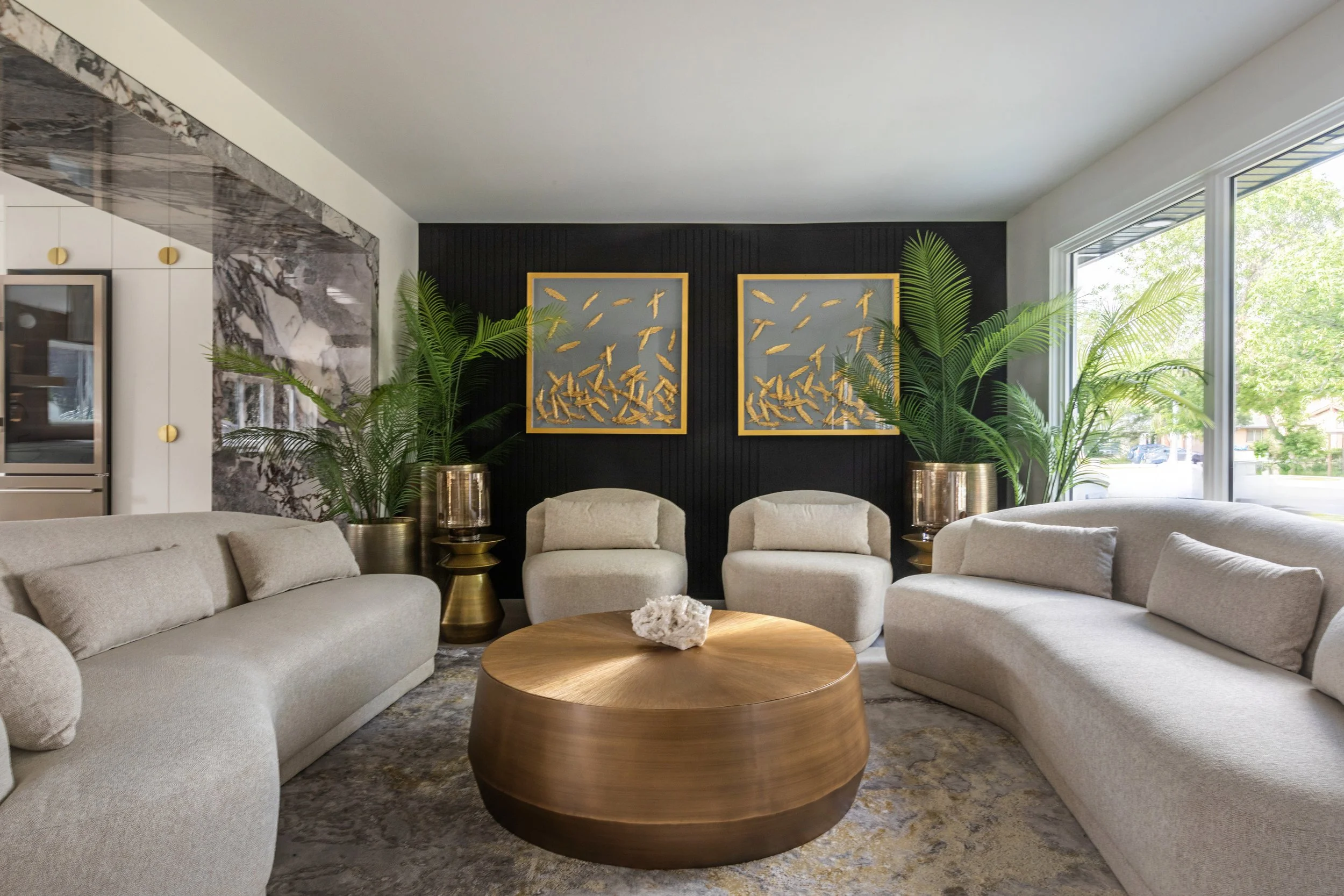 Photo of gold fish artwork hanging on a black wall above two white chairs seated in front of a gold round coffee table