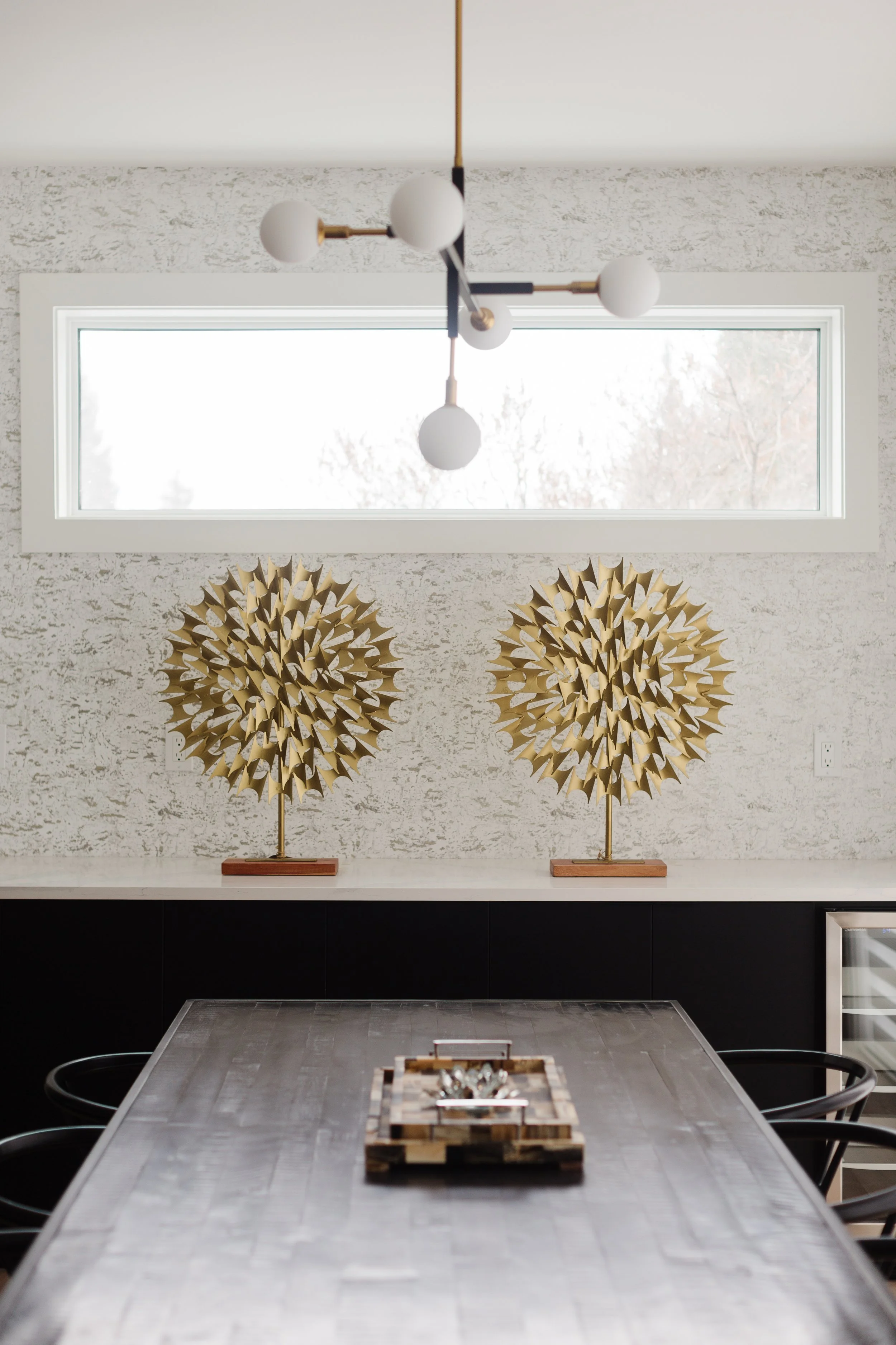 A photo of several Art Deco style interior design decor and lighting accents, including a pair of gold sculptures, modern, minimalist ceiling lighting, and decorative trays on a large table.