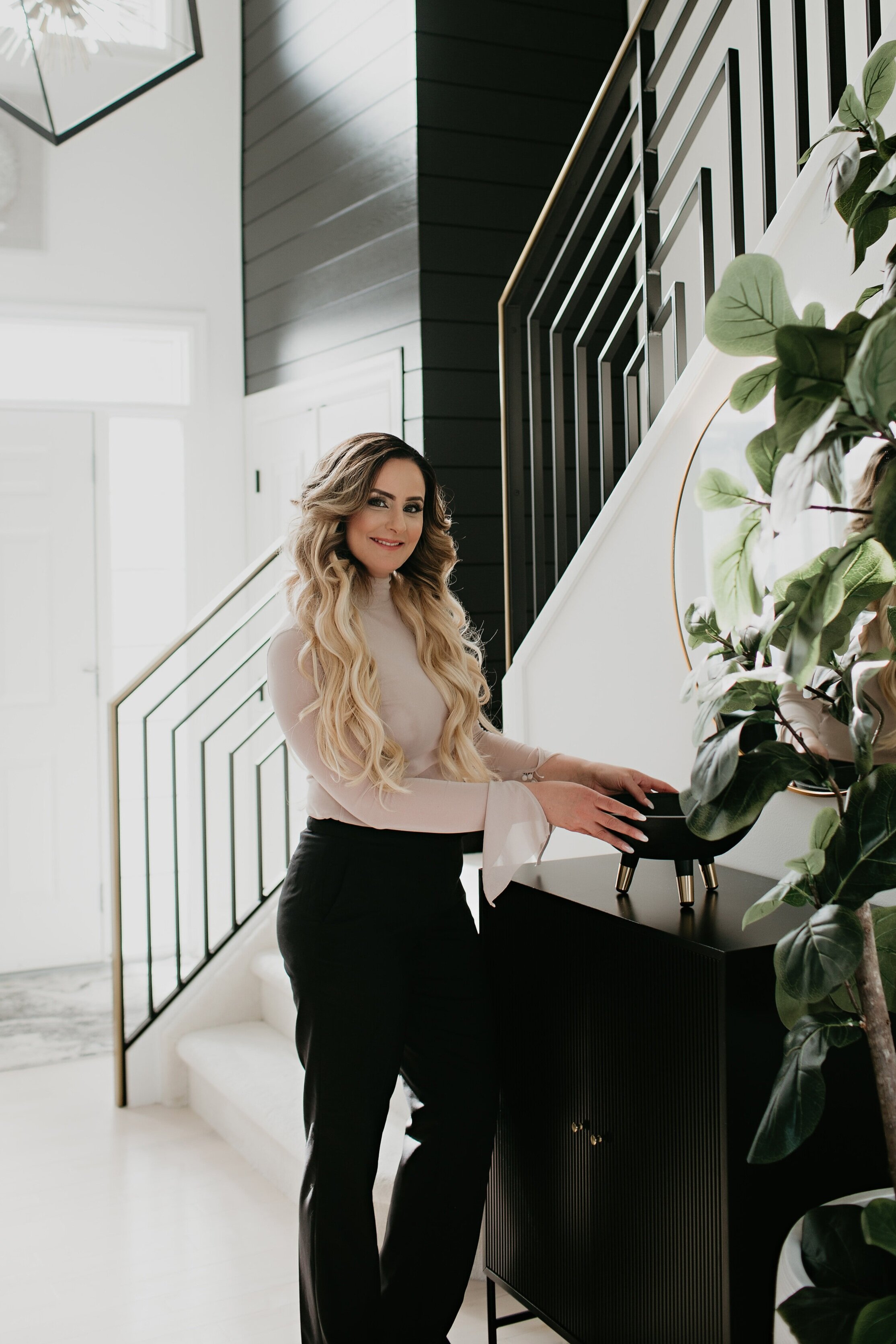Photo of woman in business attire posing next to an entryway side table while holding a bowl in a beautiful modern black and white home