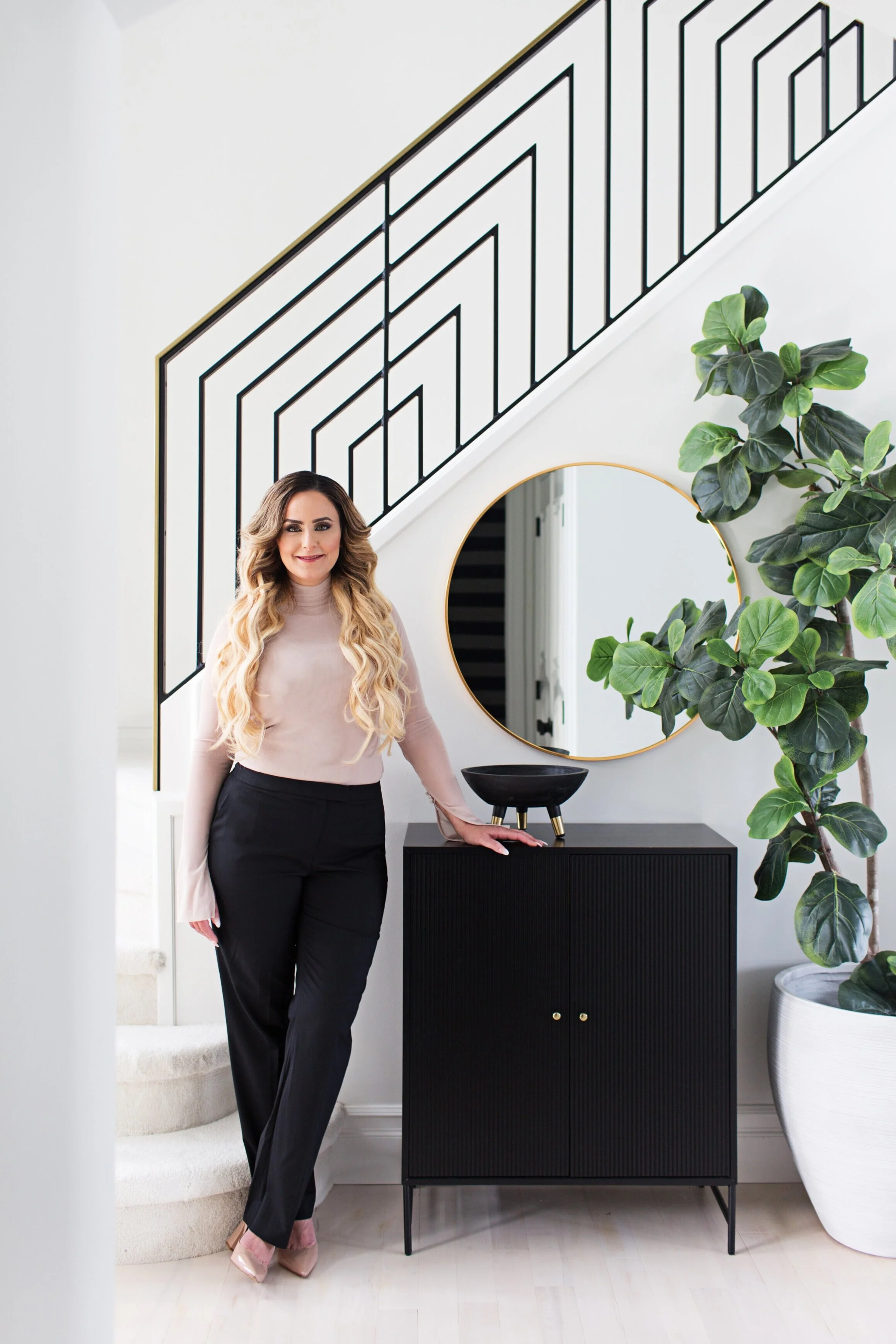 Photo of Aness Handous posing next to a black cabinet, round vanity mirror, and houseplant in front of staircase