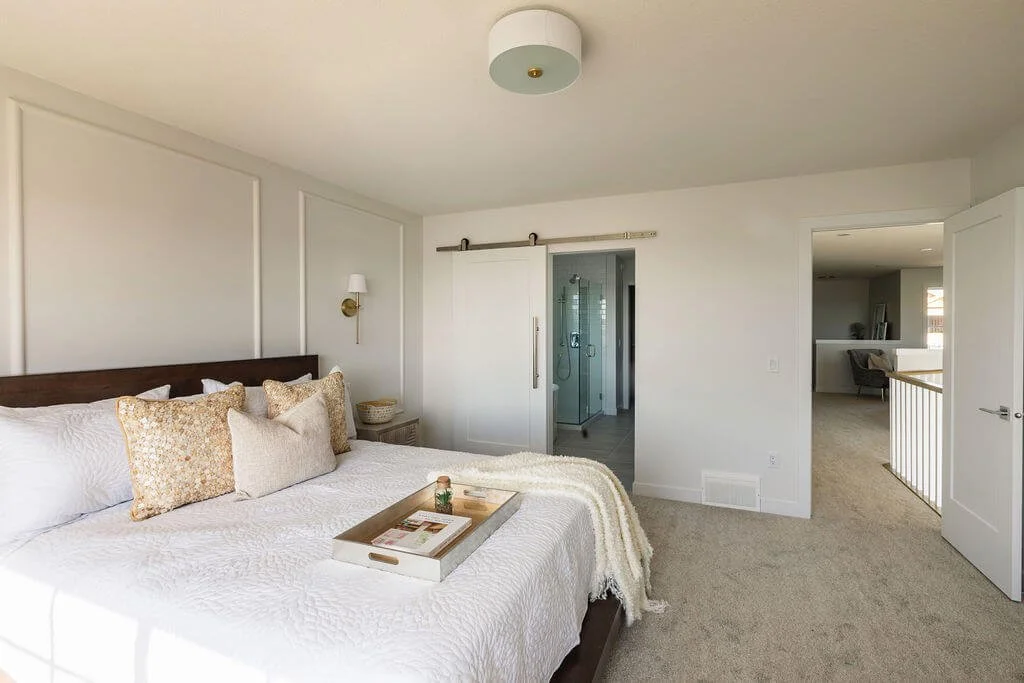 Photo of a white bedroom with a white bed, throw pillows, a blanket, and a tray next to an open door leading to a bathroom, showing the best tips for minimalist bedrooms