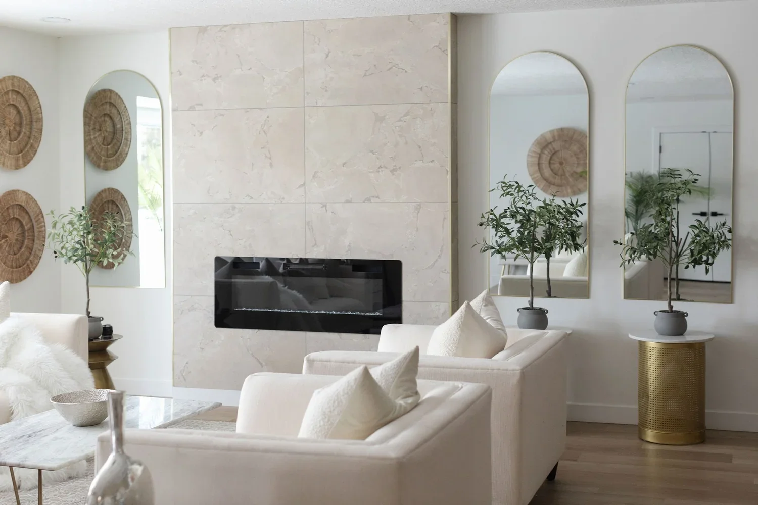 photo of a luxury living room with a white marble wall and fireplace next to mirrors and facing white sofas