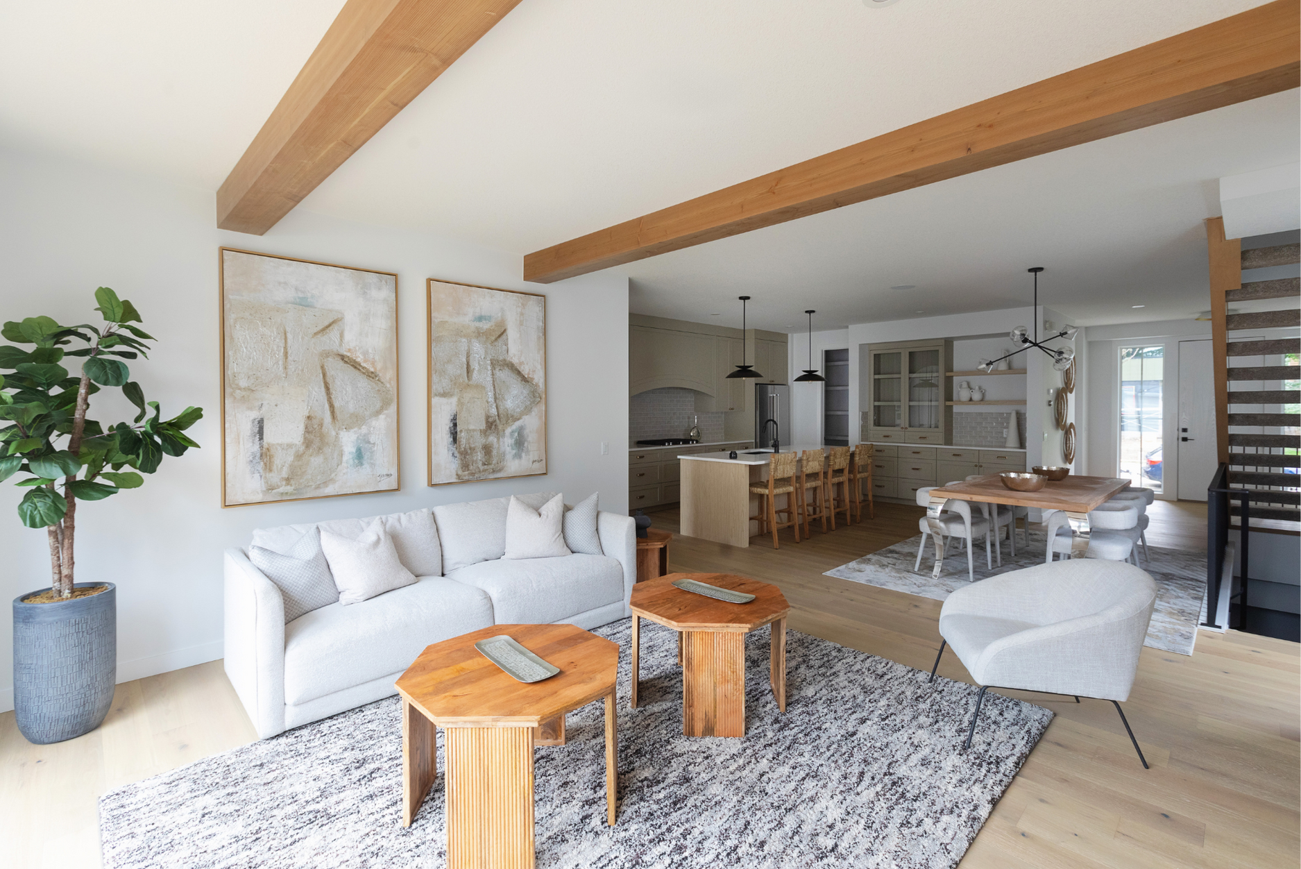 Photo of an open-concept dining and living area with wood furniture and wood beams, plus modern white furniture and artwork