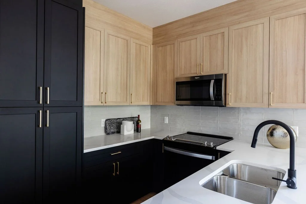 Photo of a kitchen with brown and black cabinets and white granite countertops with some decor