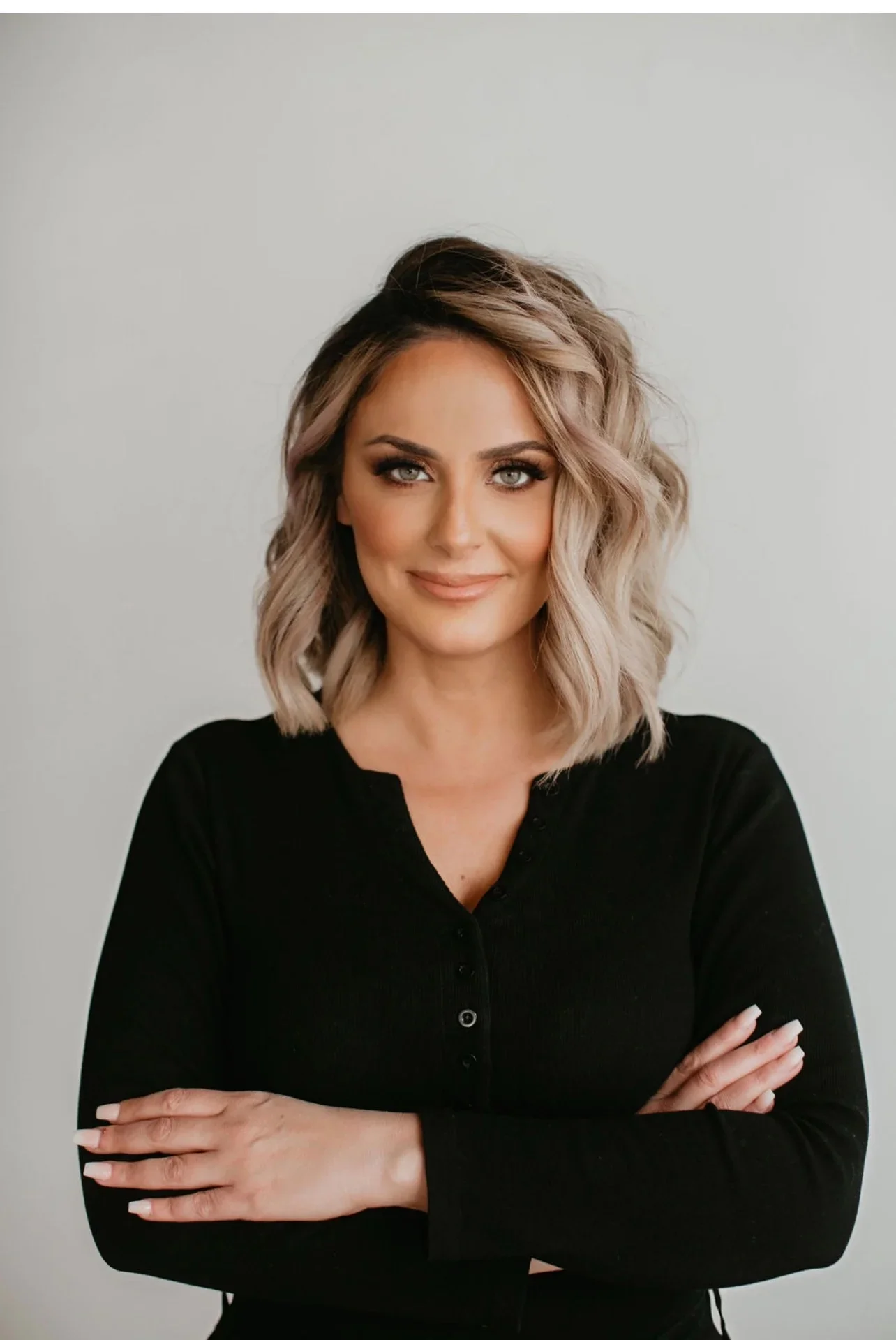 Headshot of Aness Handous a woman smiling in a black shirt with her arms crossed against a neutral background