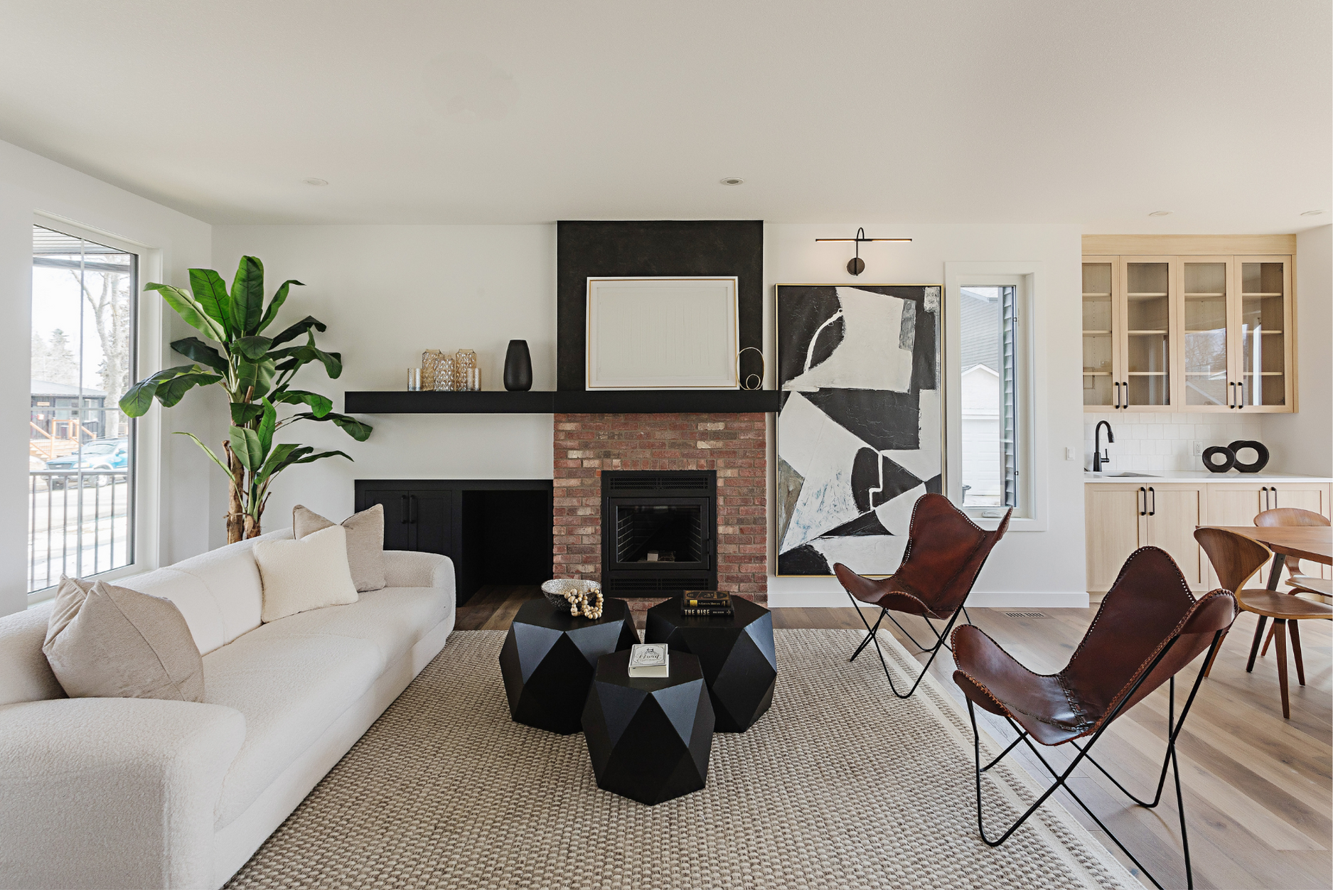 An image of a contemporary living room with a white sofa, black geometric coffee tables, leather chairs, and a brick fireplace styled with the best materials for sustainable interiors
