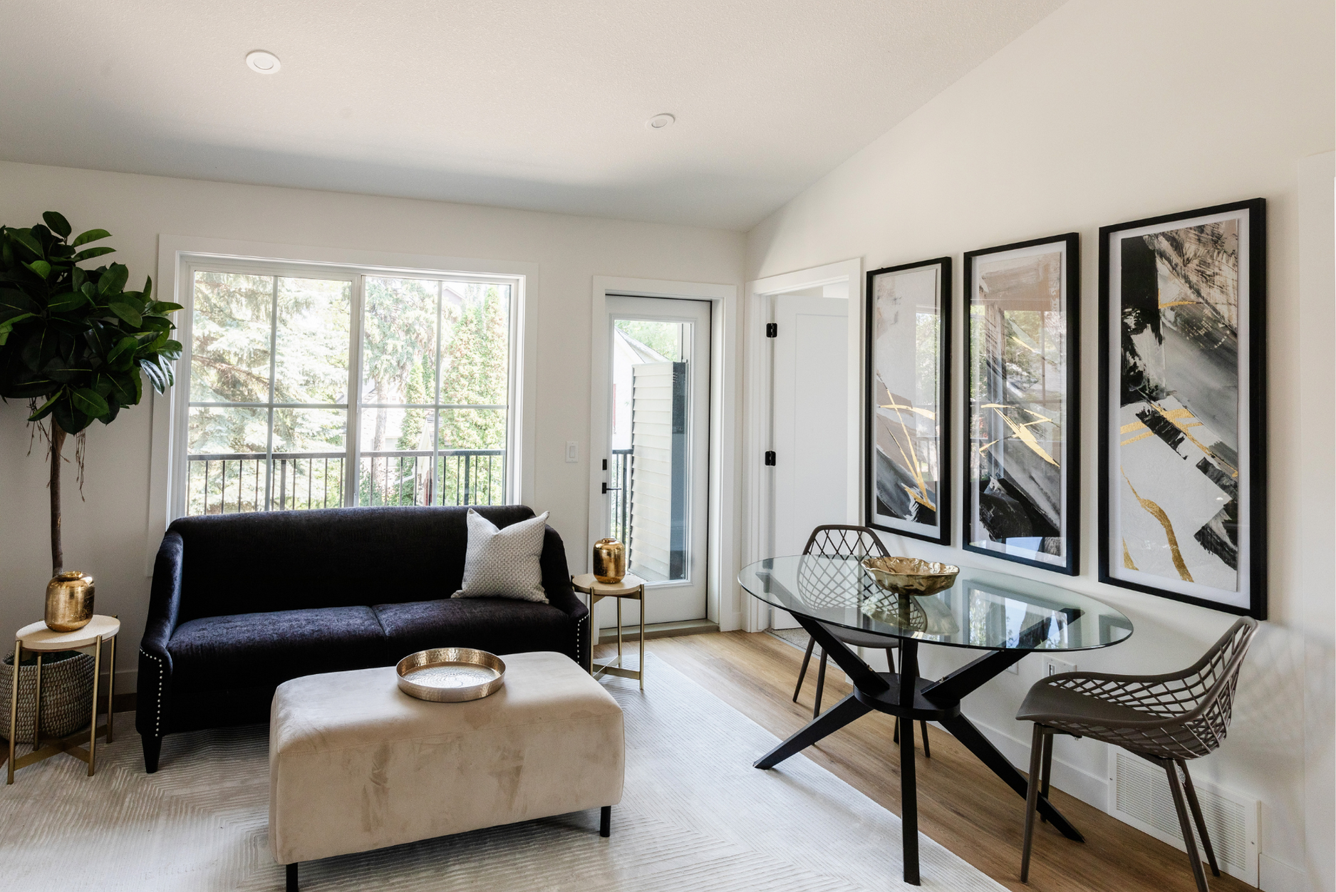 Photo of a white living room with furniture, gold decor, and a glass table below black and gold artwork pieces