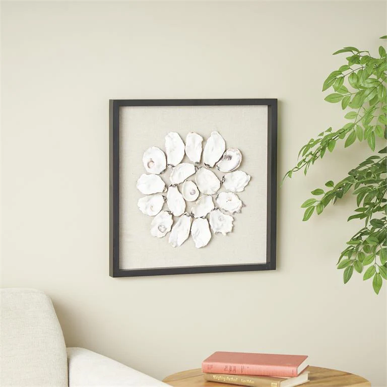 Photo of seashell artwork hanged on a white wall next to a houseplant and above a table and chair showing what is coastal interior