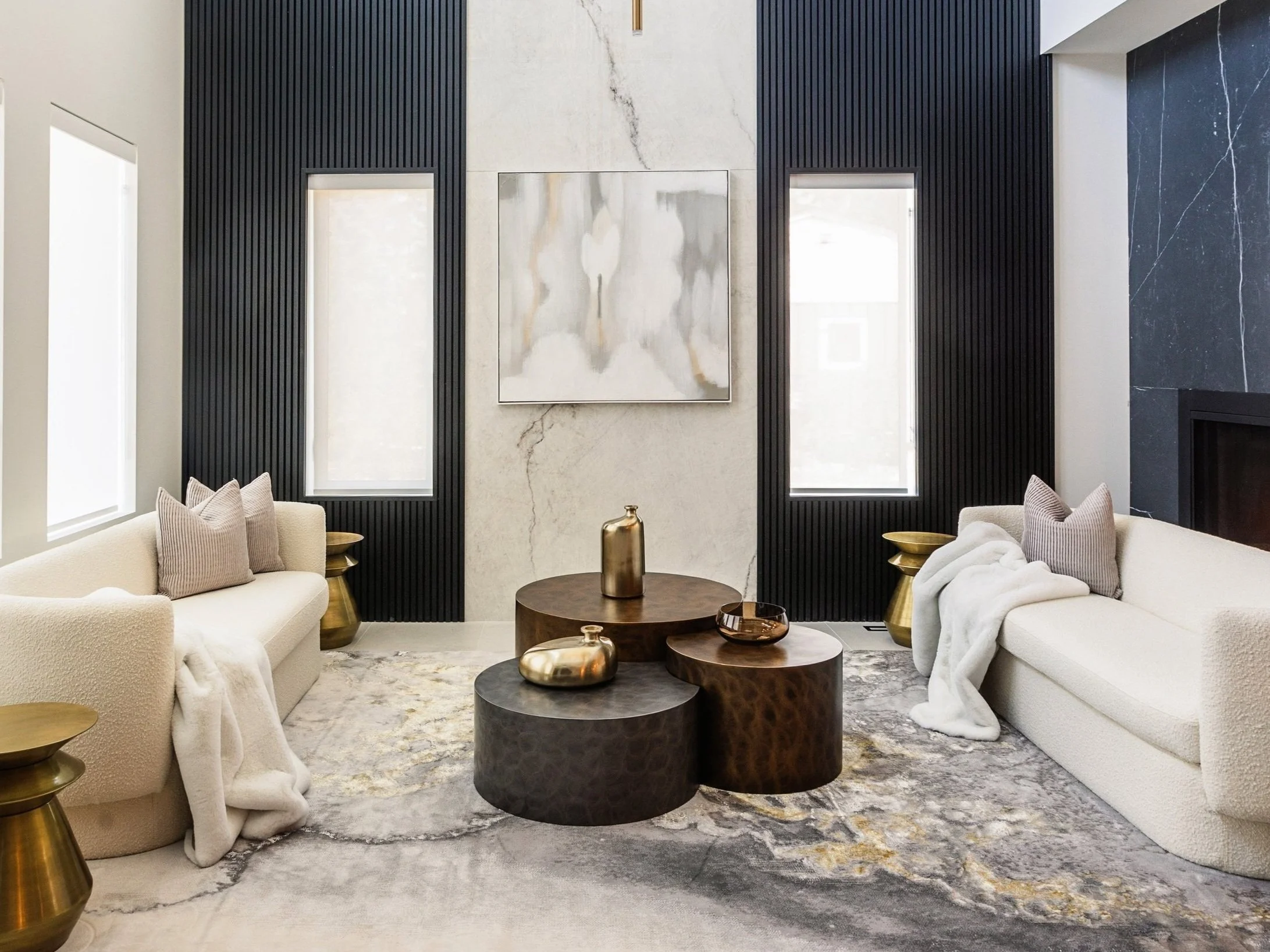 Photo of luxury home decor Edmonton furniture staged in a living with white marble walls, white sofas facing smooth cylindric tables, and gold accents on a grey and gold marble rug