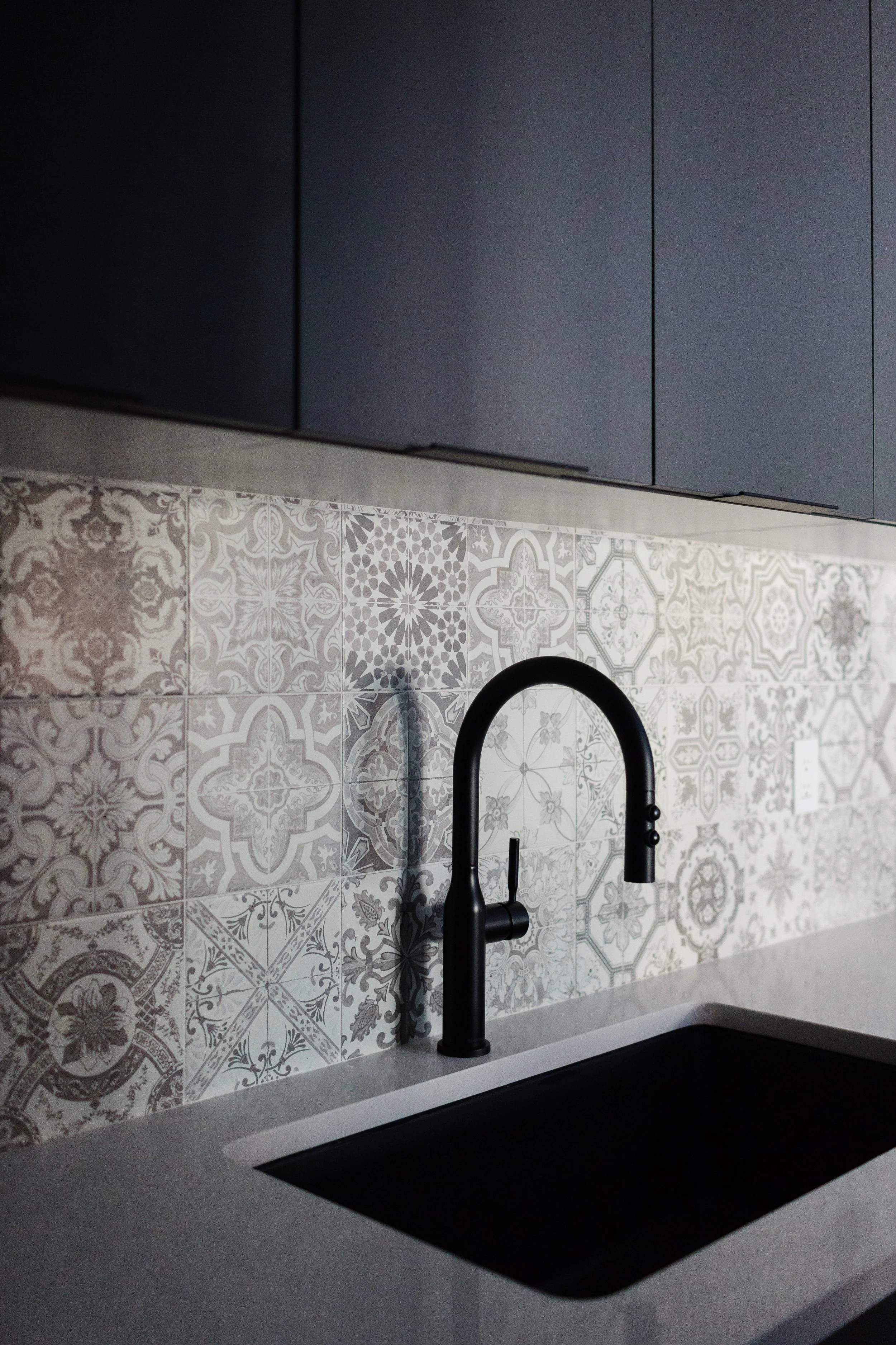 An image of a modern kitchen with a patterned tile backsplash and matte black faucet