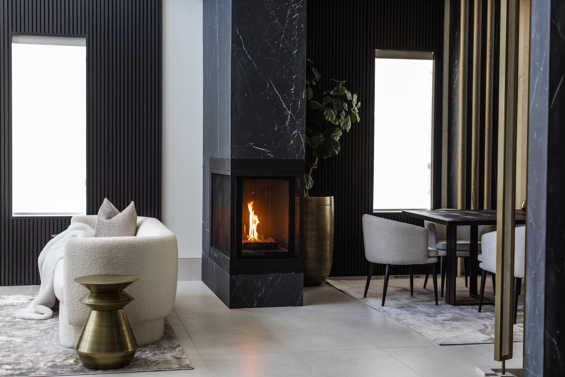 A photo of a transitional space between living and dining room outfitted with a stone-wrapped fireplace feature, flanked by textural wall panelling and upholstered furniture.