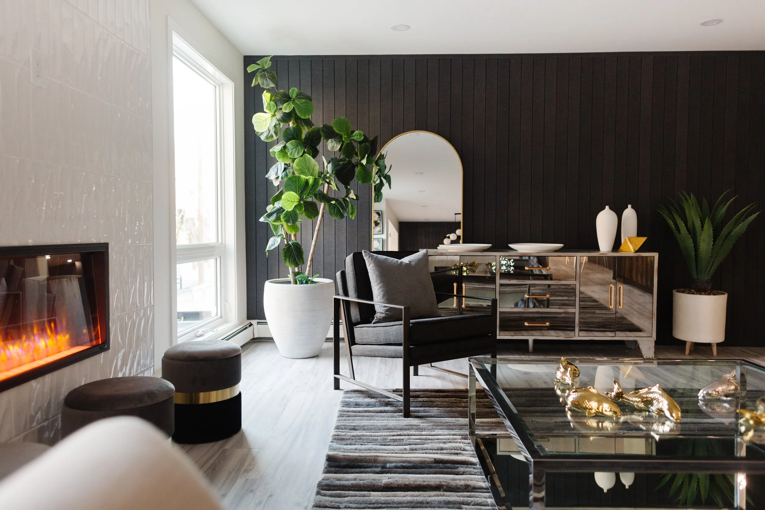 Photo of a living room with black furniture, plant decor, and a large glass coffee table next to an electric fireplace