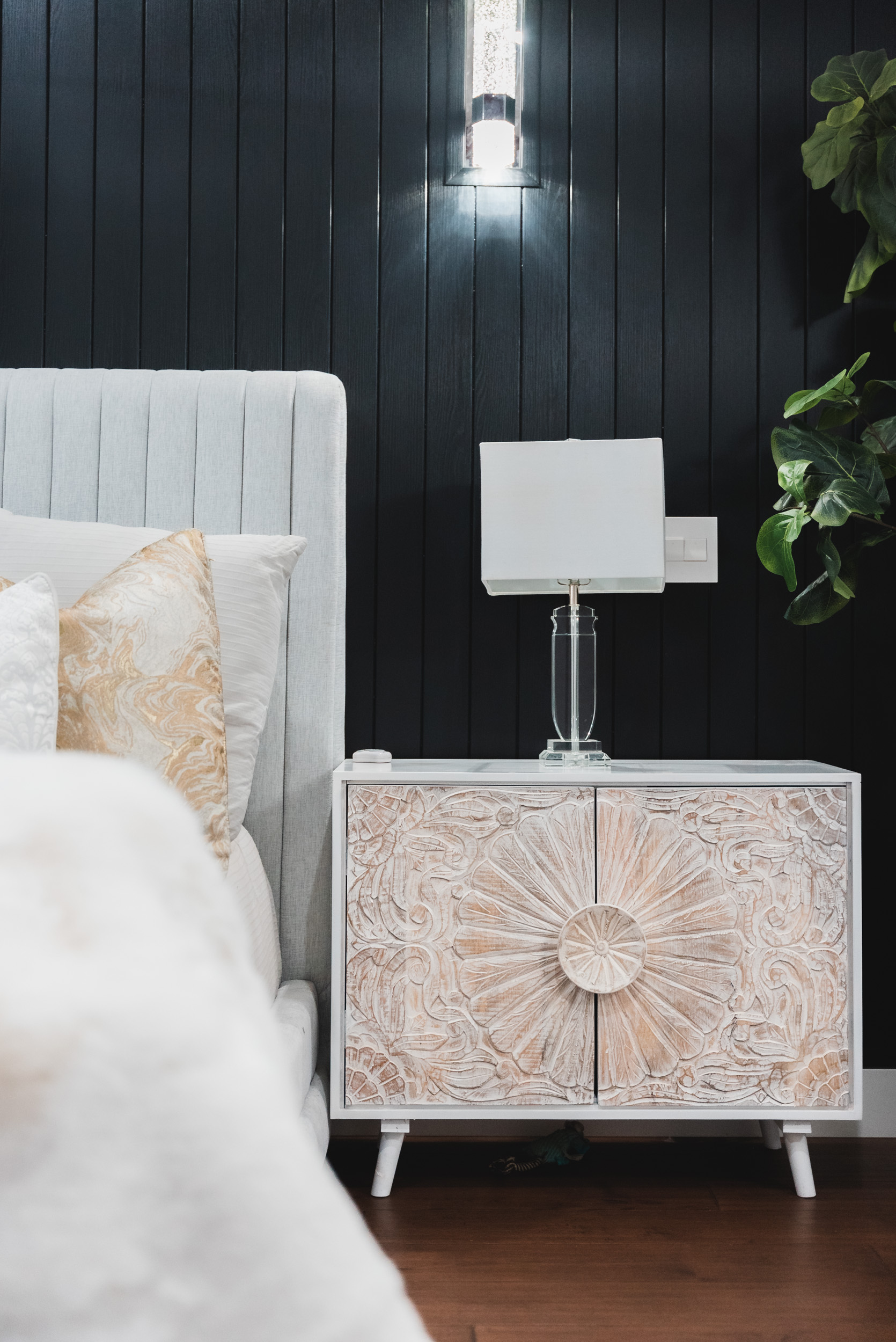 Pphoto of a seashell nightstand with white glass lamp on top next to white bed