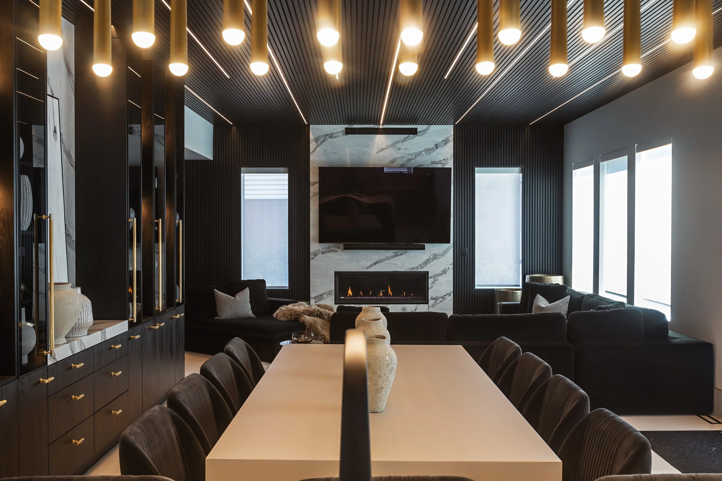 Picture of a large open-concept dining and kitchen area featuring a long white dining table with black chairs under a black slatted ceiling with recessed lighting