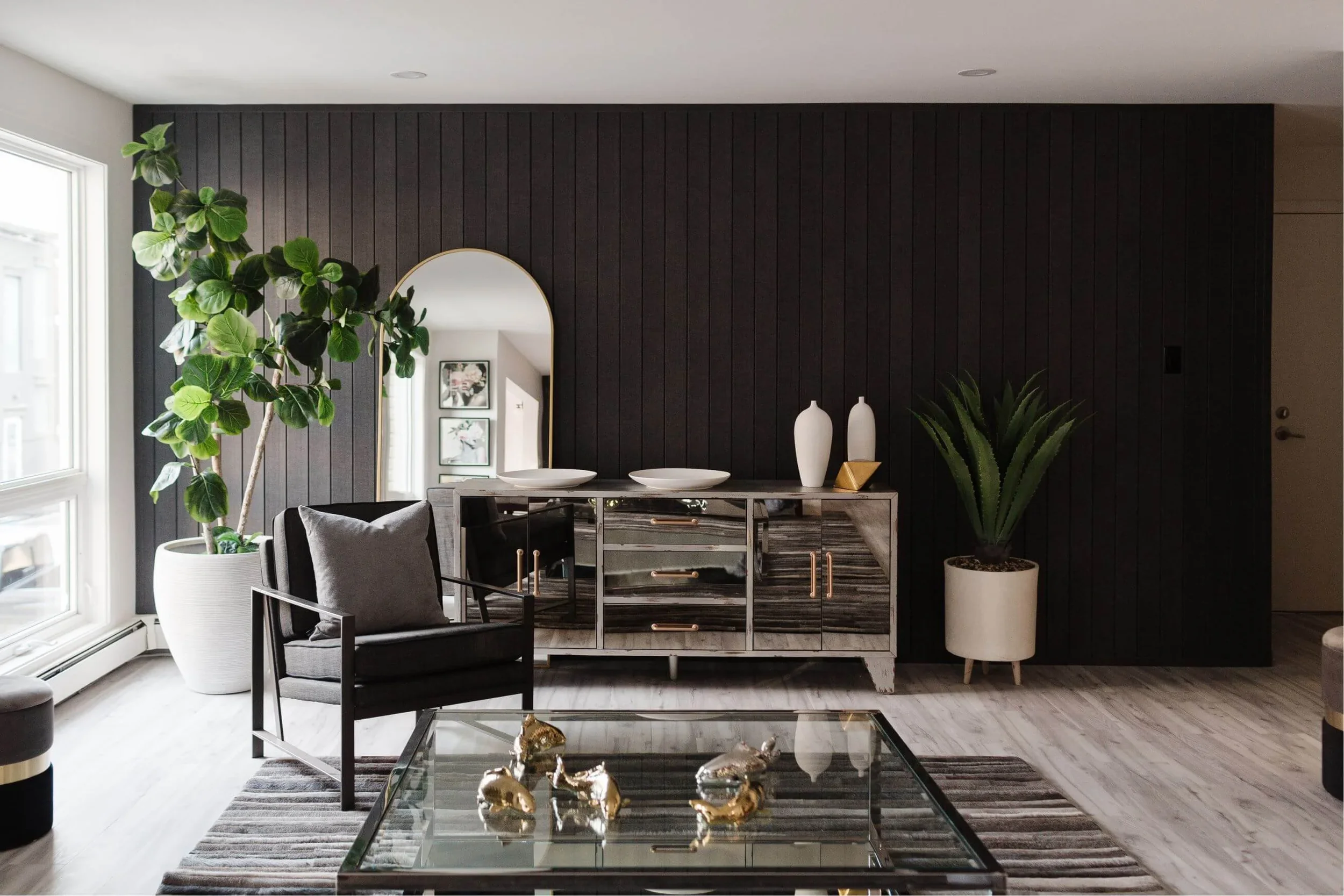 photo of a modern black living room with a reflective side board facing a black armchair and glass coffee table with gold decor on top