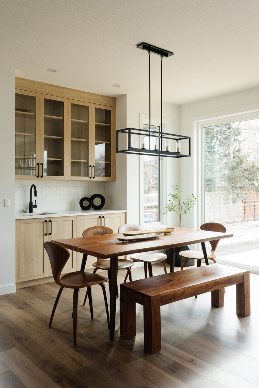 Photo of a dining room with a wood dining table and chairs beneath a black light fixture in front of a wood sideboard and shelving