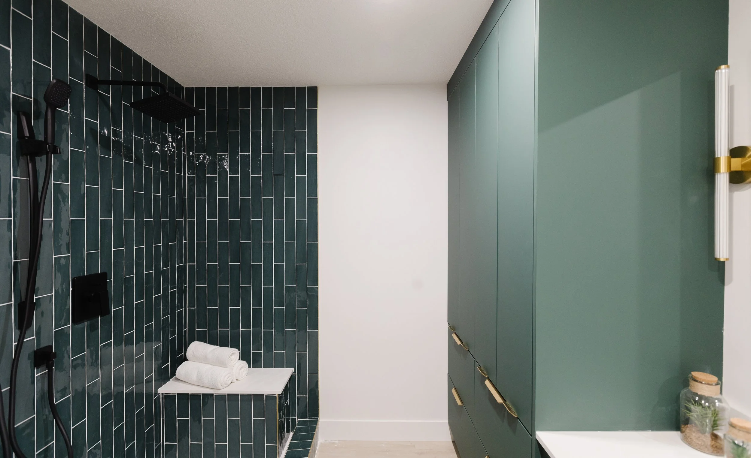 Photo of a teal-coloured bathroom with a teal tiled stand-up shower facing a teal green cabinet with gold fixtures
